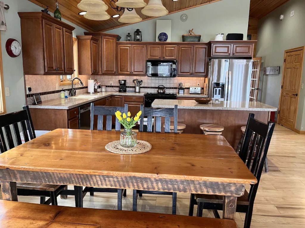 A kitchen with a wooden table and chairs and a vase of flowers on the table.