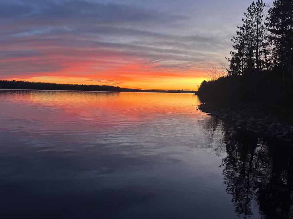 A sunset over a lake with trees on the shore