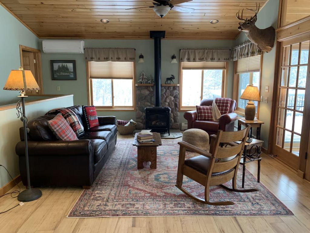 A living room with a couch , chairs , lamps and a deer head on the wall.