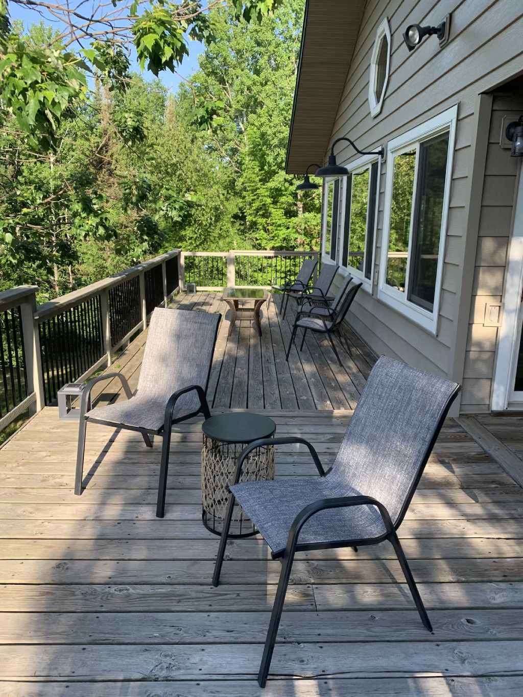There are two chairs and a table on the deck of a house.