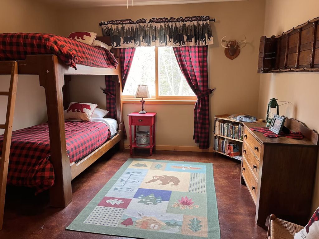 A bedroom with bunk beds , a rug , a dresser and a window.