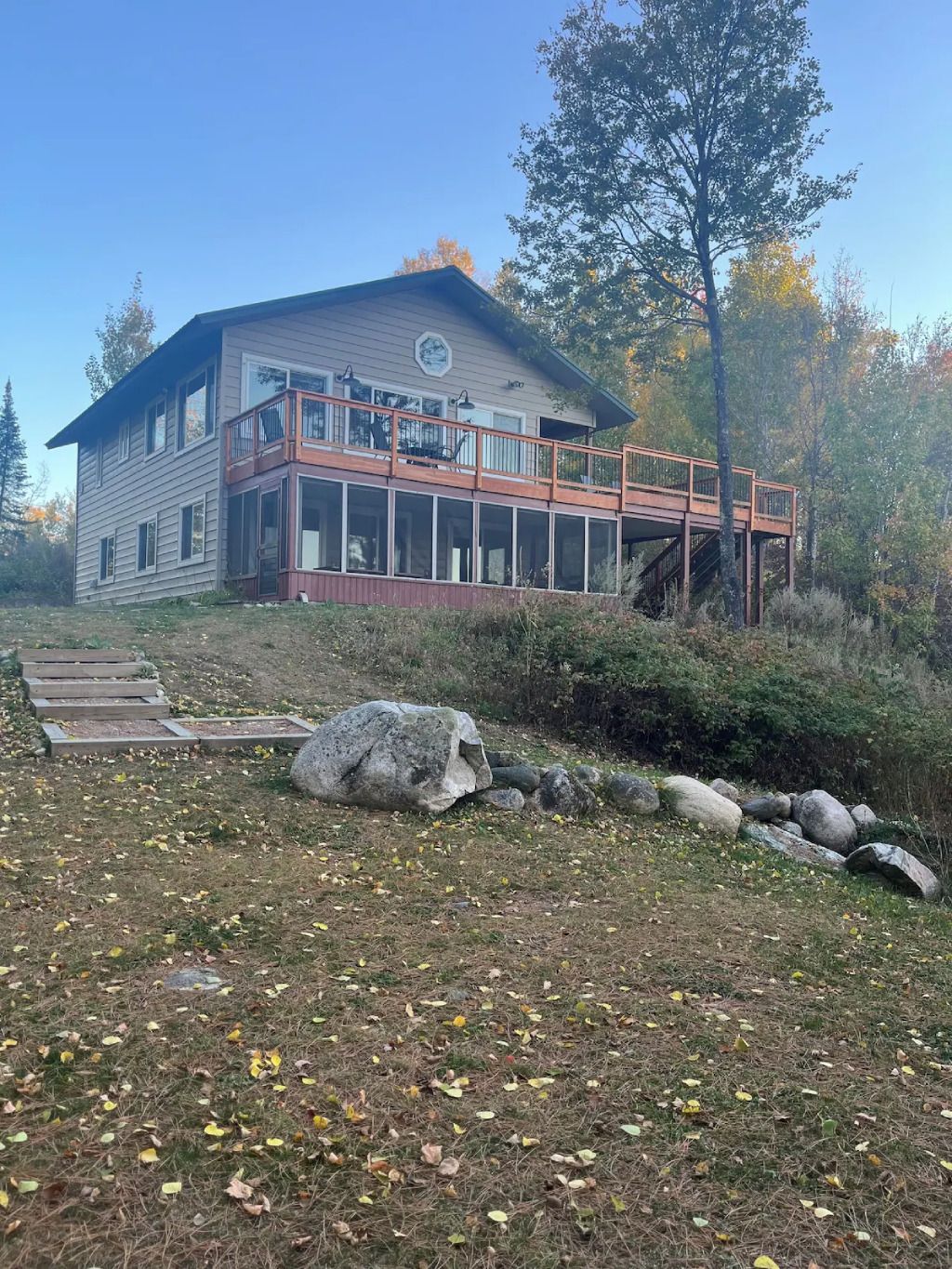 A large house with a large deck in the middle of a field surrounded by trees.