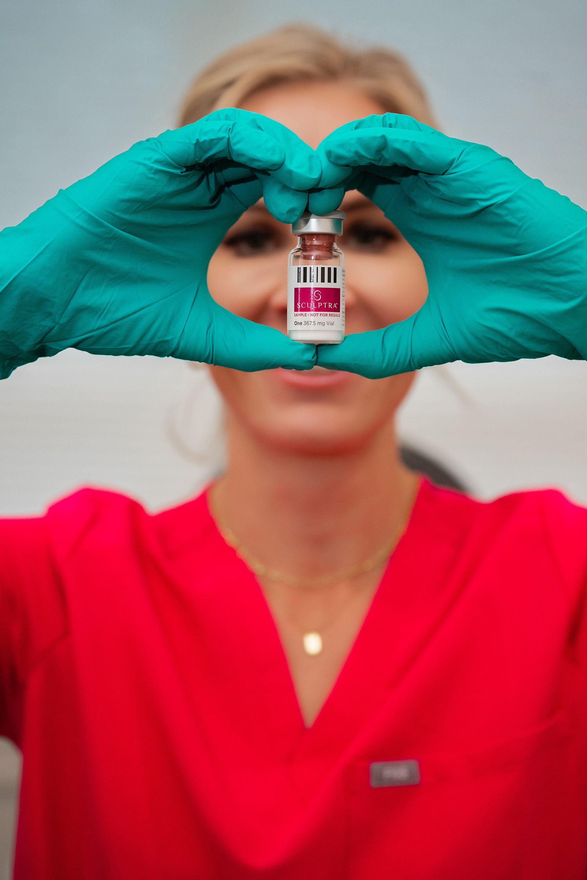 a woman wearing green gloves is holding a bottle of vaccine in front of her face .