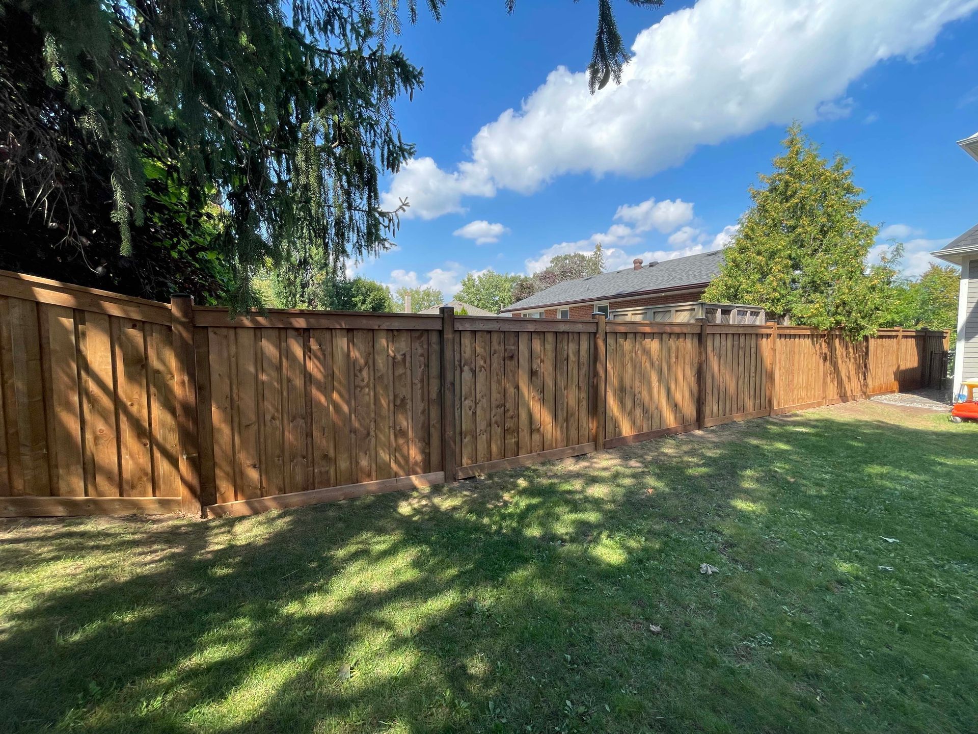 A wooden fence surrounds a lush green lawn in a backyard.