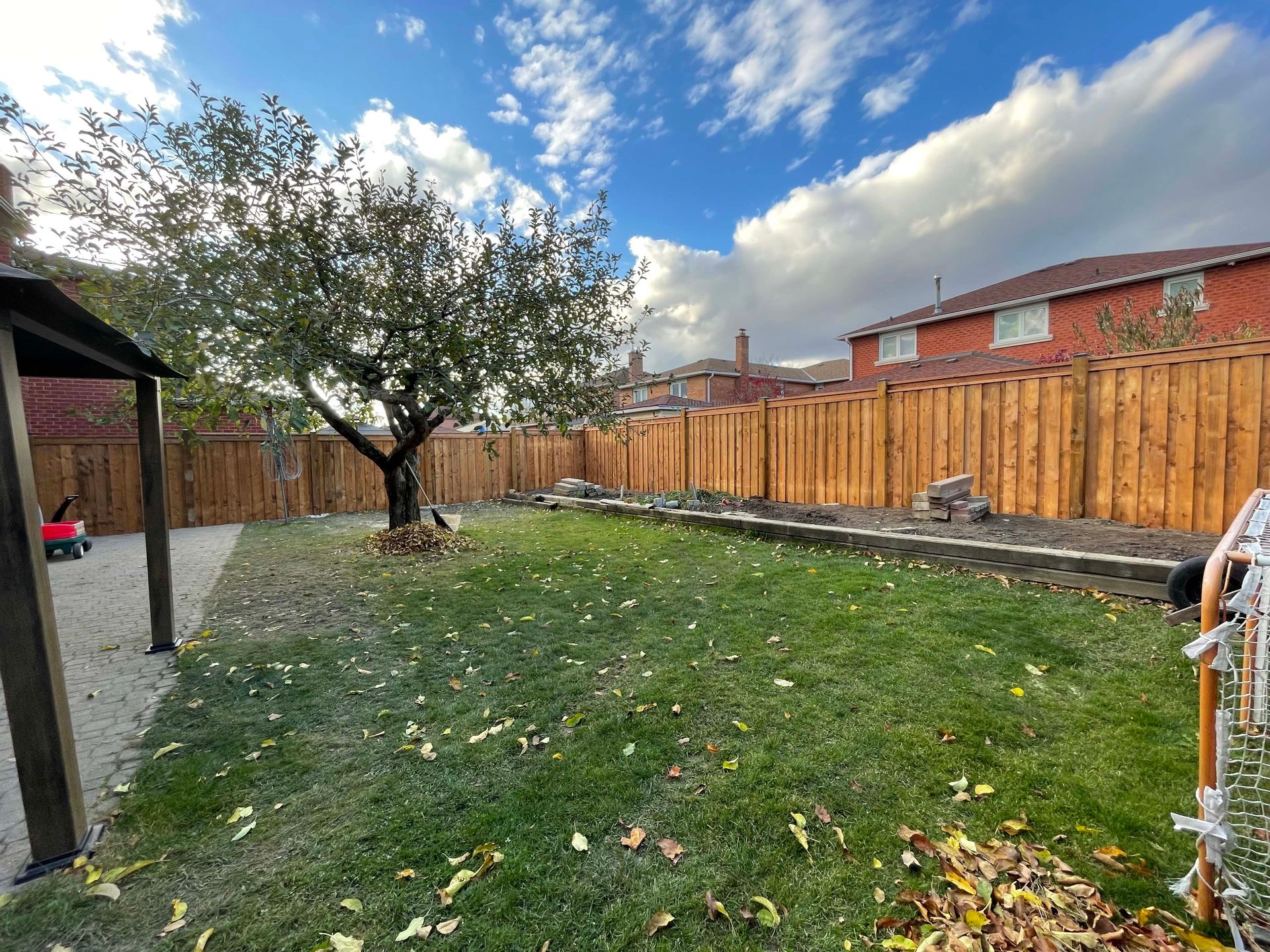 A backyard with a wooden fence and a tree.