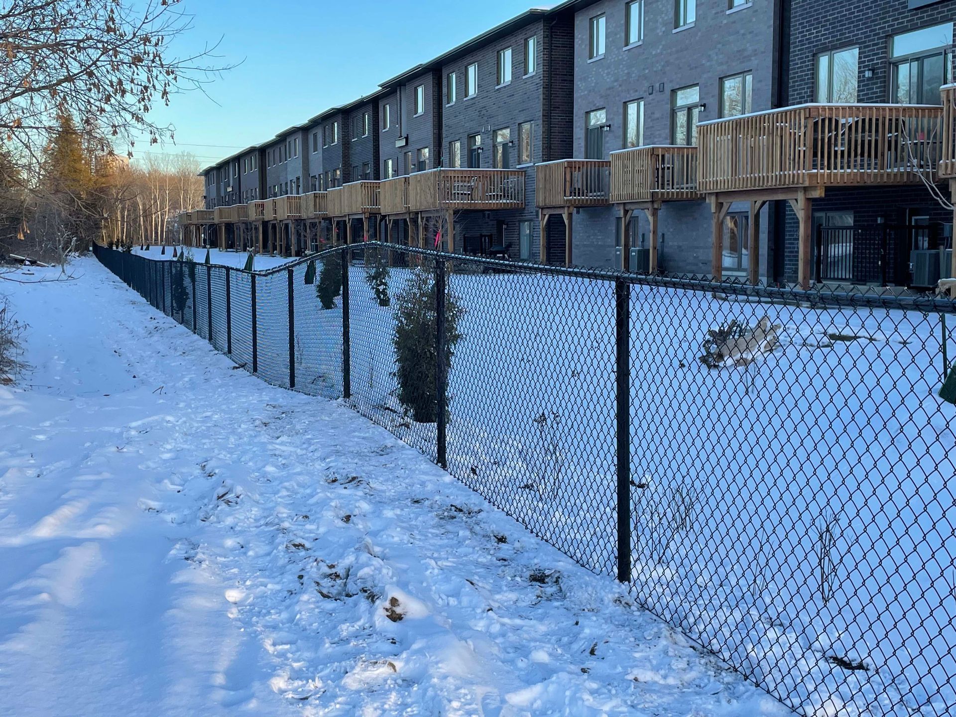 A chain link fence is surrounded by snow in front of a row of houses.