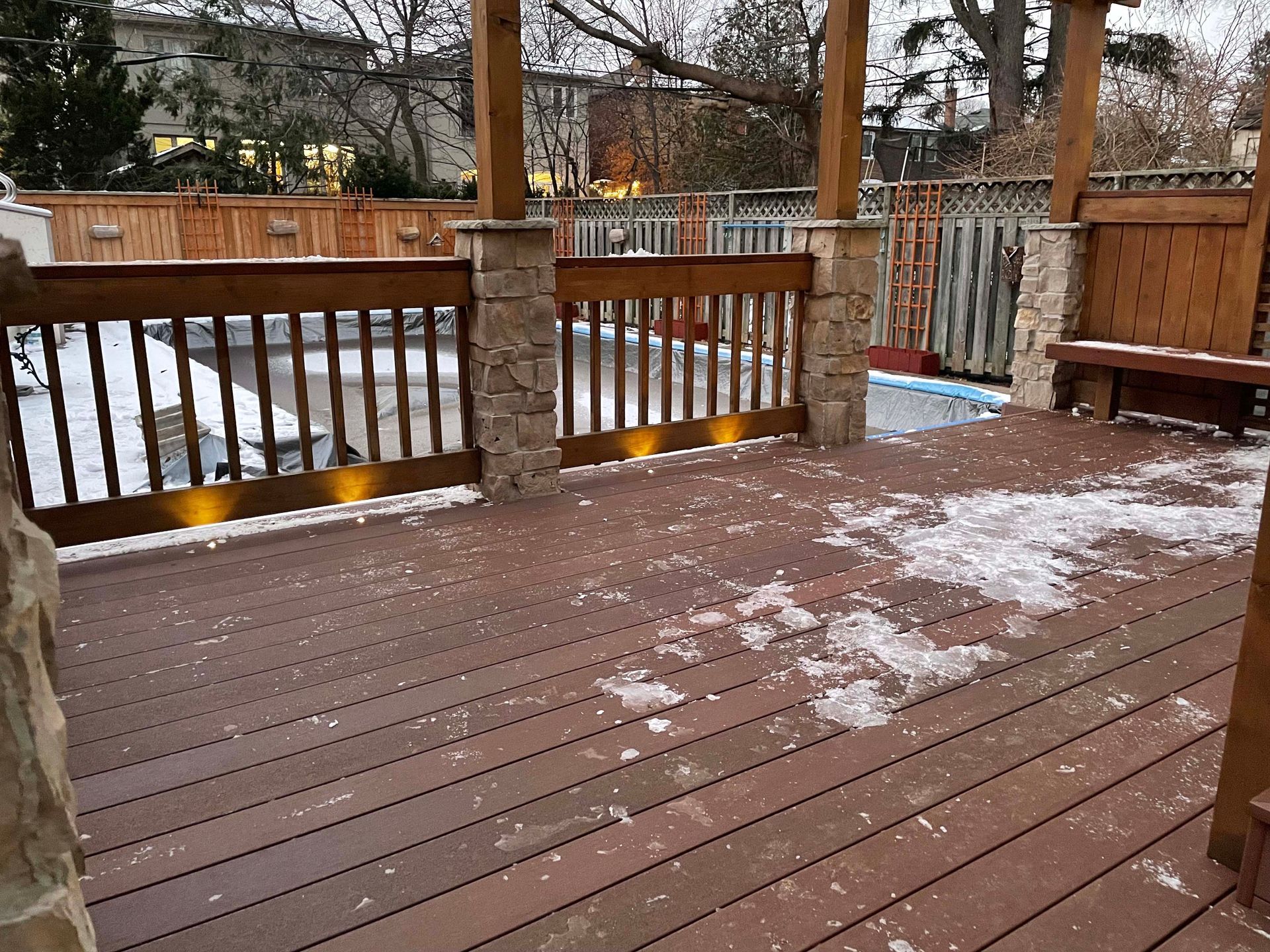 A deck with a wooden railing and a bench in the snow.