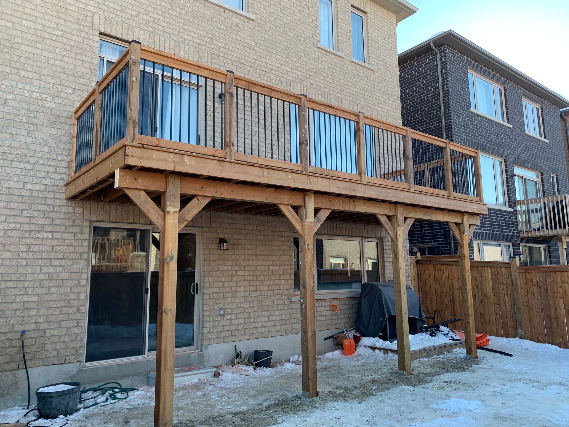 A wooden deck is sitting in the backyard of a brick house.