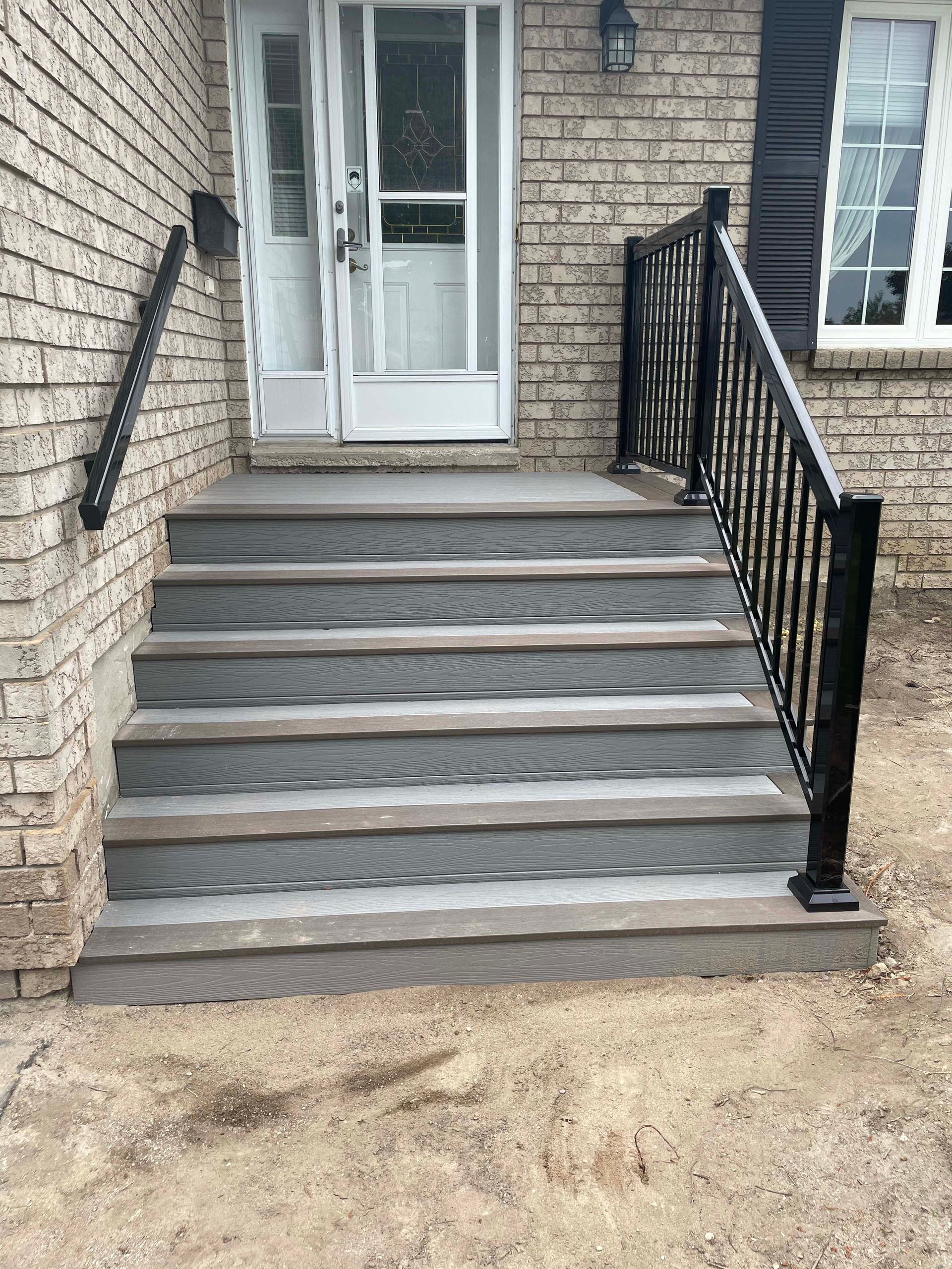 A set of stairs leading up to a brick house with a black railing.