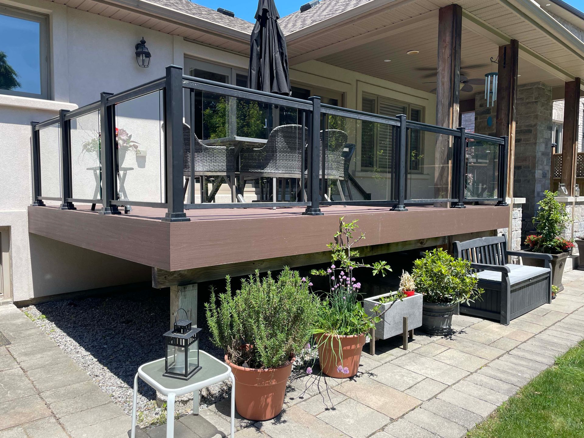 A large deck with a glass railing and potted plants in front of a house.