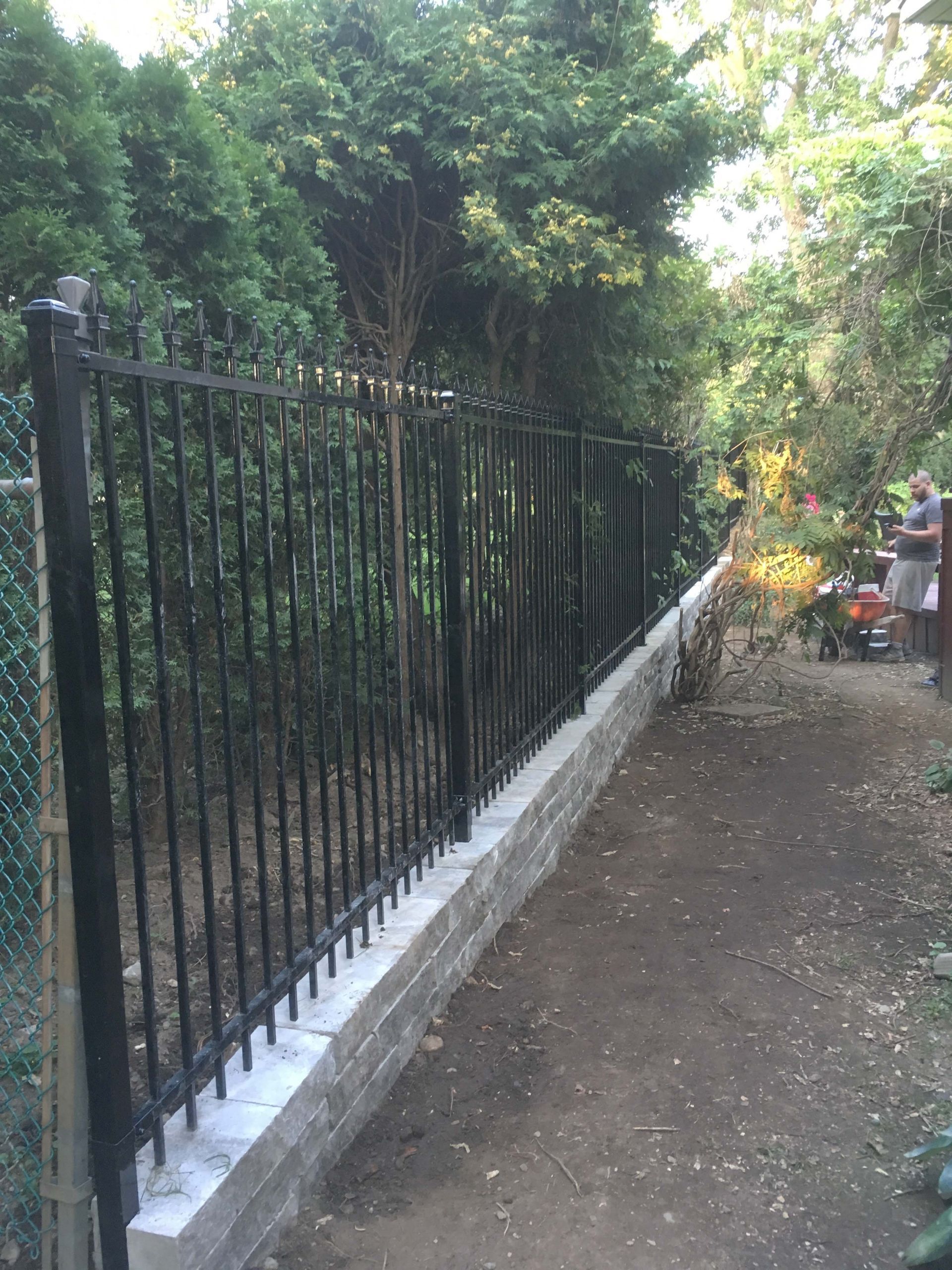 A black fence is surrounded by trees and a path.