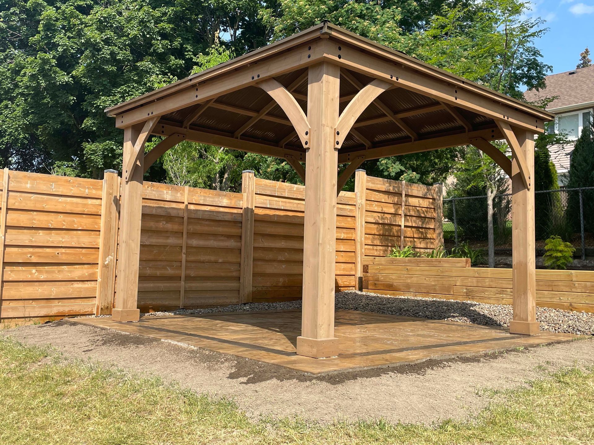 A wooden gazebo in a backyard next to a wooden fence.