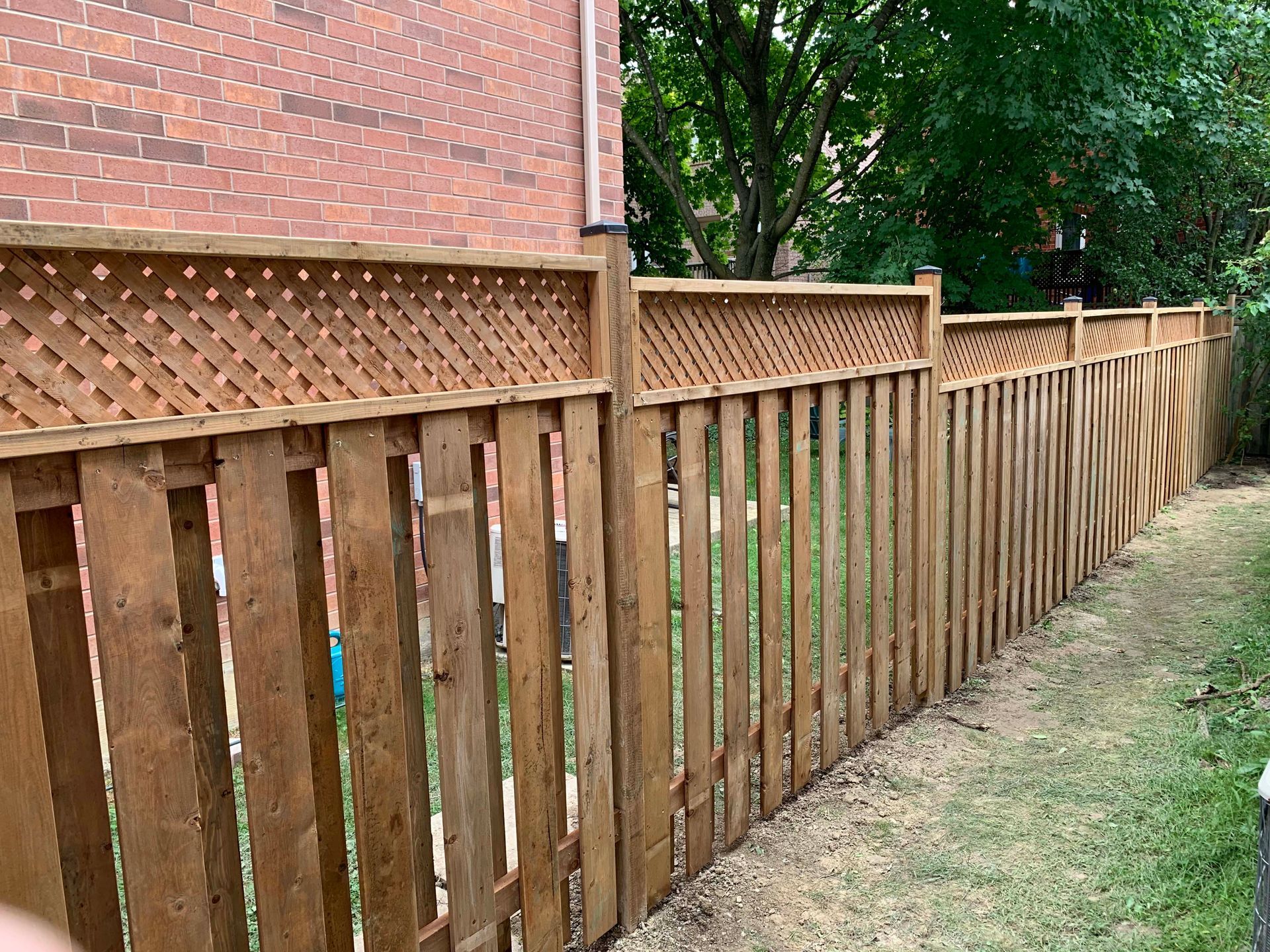 A wooden fence with a lattice top is in a backyard next to a brick building.
