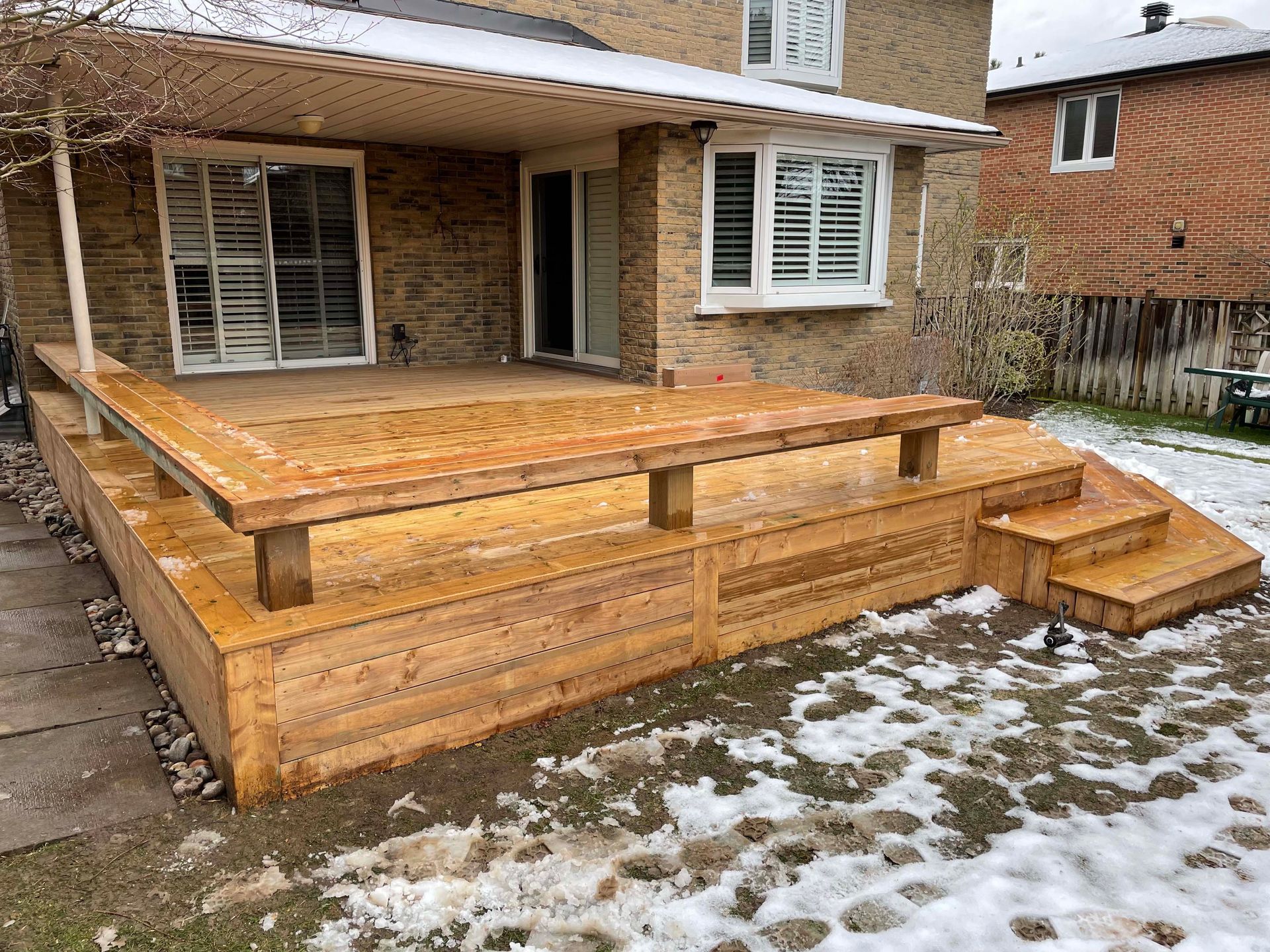 A wooden deck with stairs is in front of a brick house.