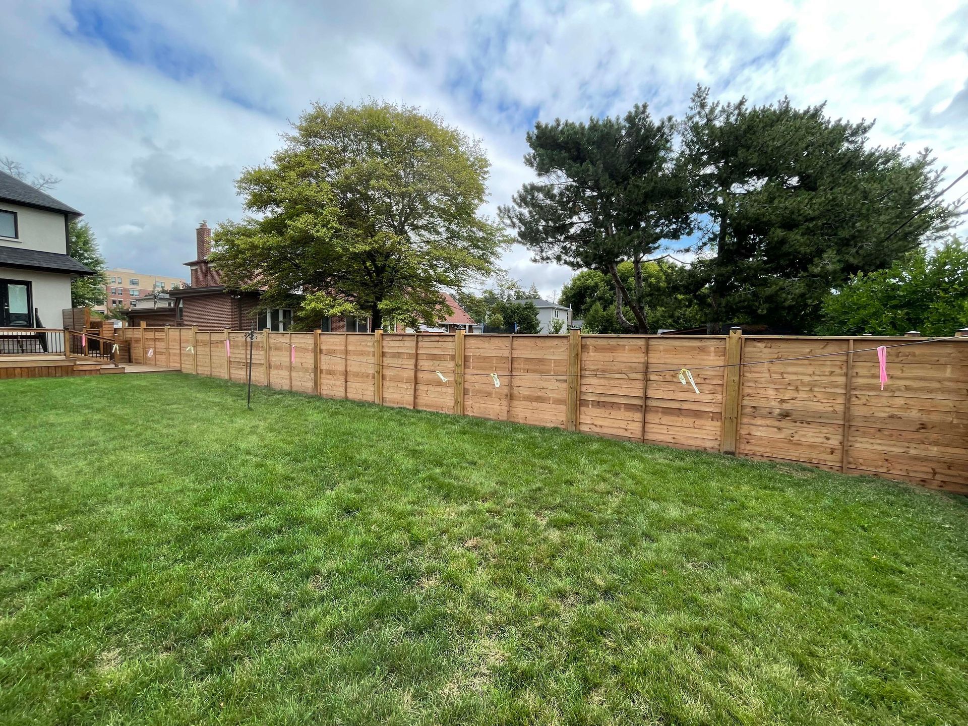 A wooden fence surrounds a lush green lawn in a backyard.