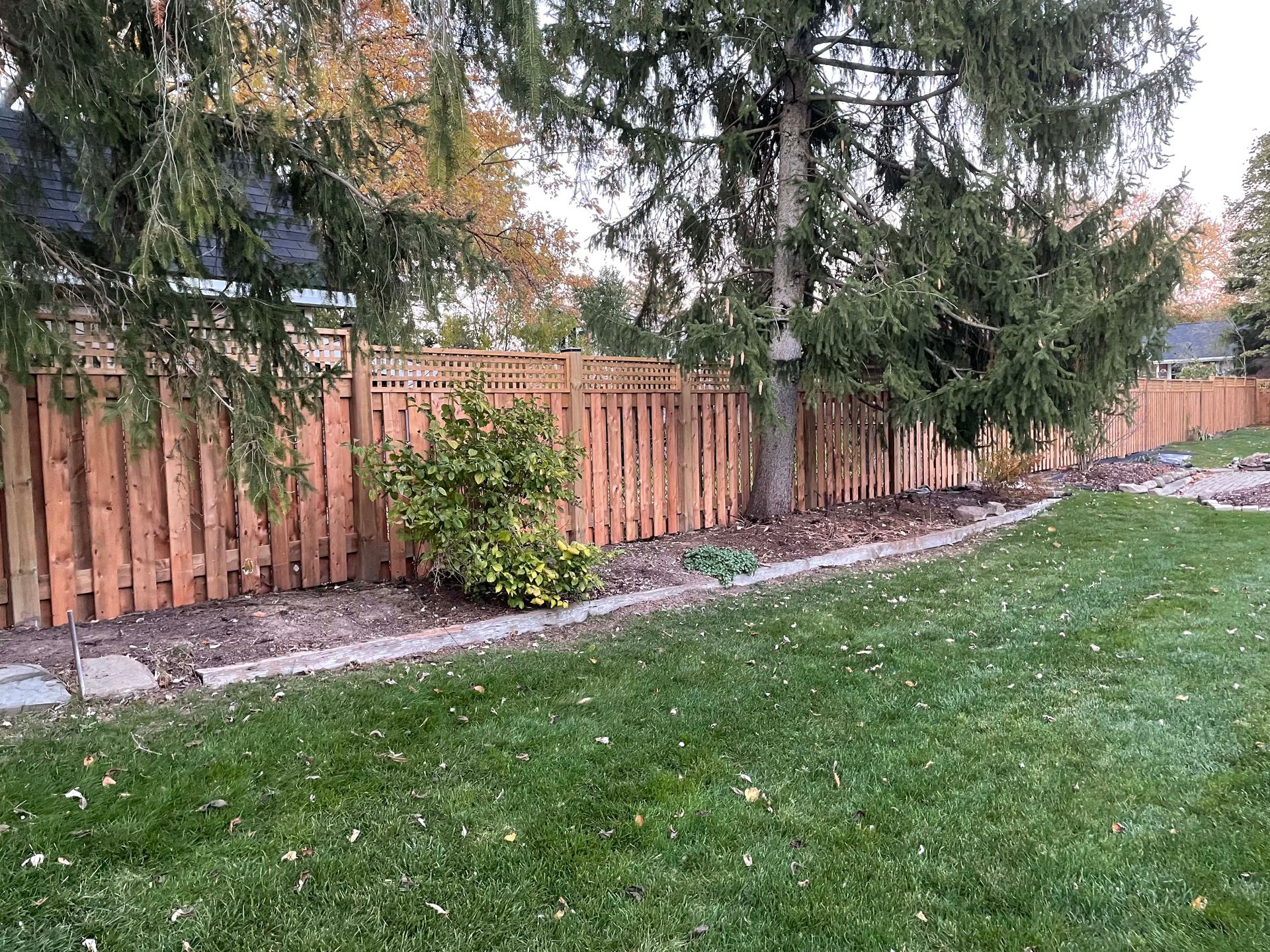 A wooden fence surrounds a lush green lawn in a backyard.