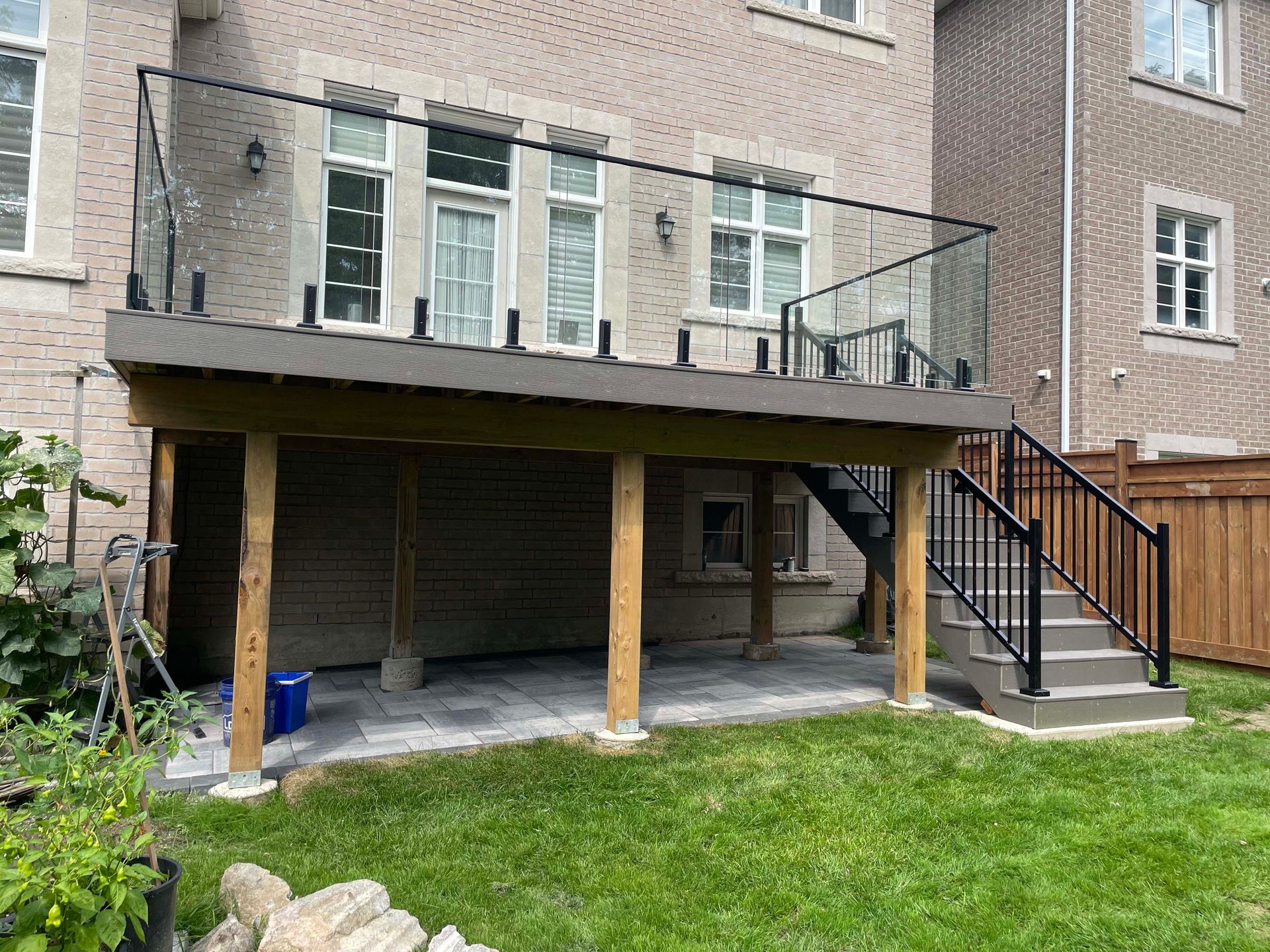 A deck with stairs and a glass railing in the backyard of a house.