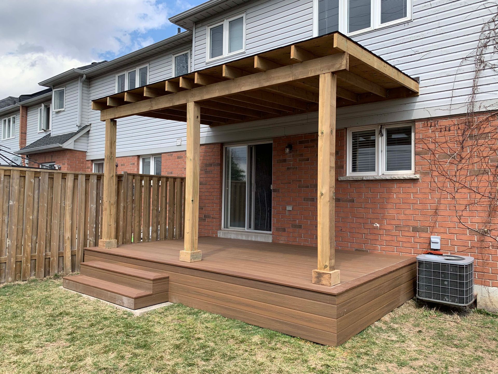 A wooden deck is sitting in the backyard of a brick house.
