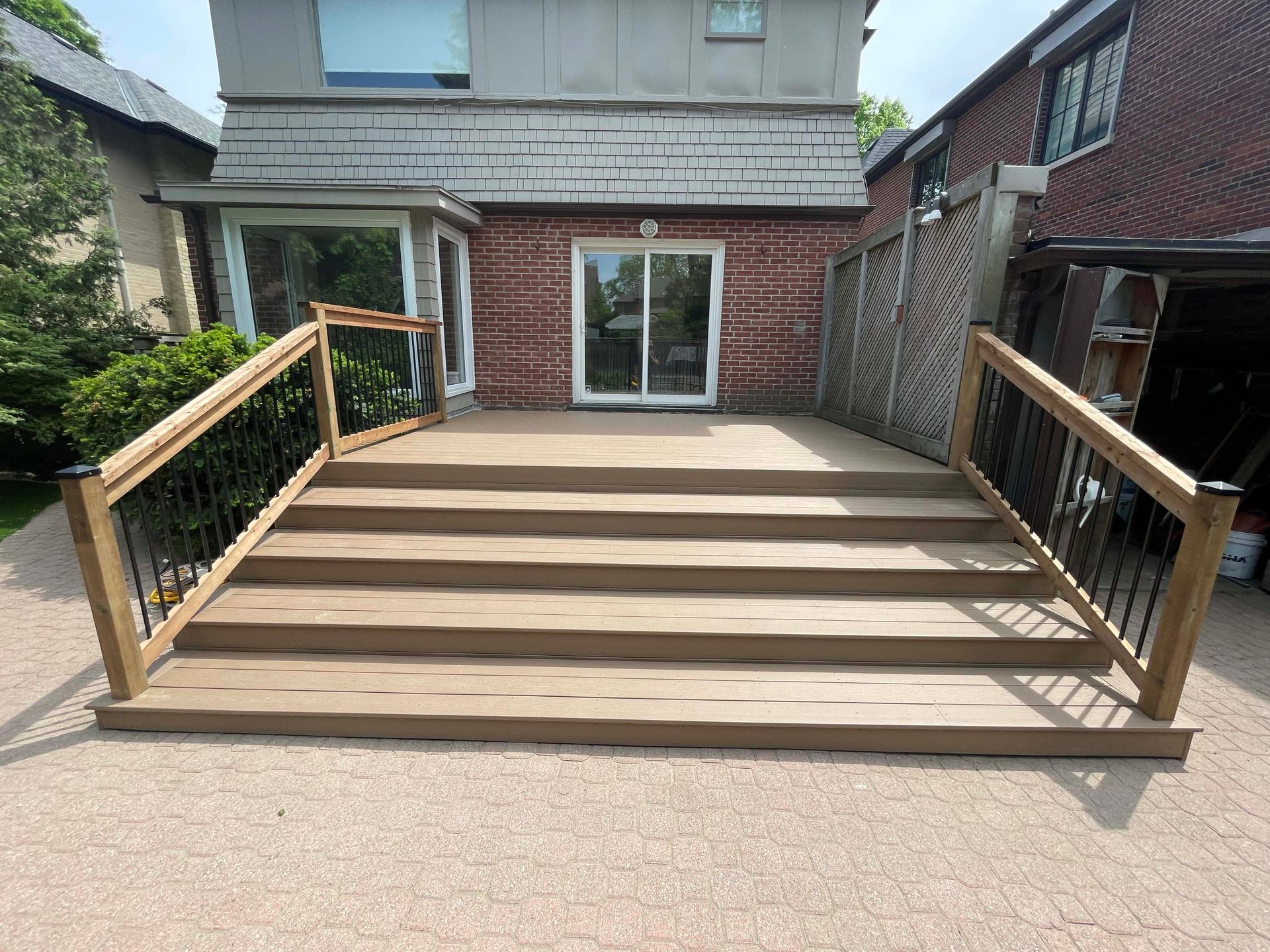 A wooden deck with stairs and a railing in front of a brick house.