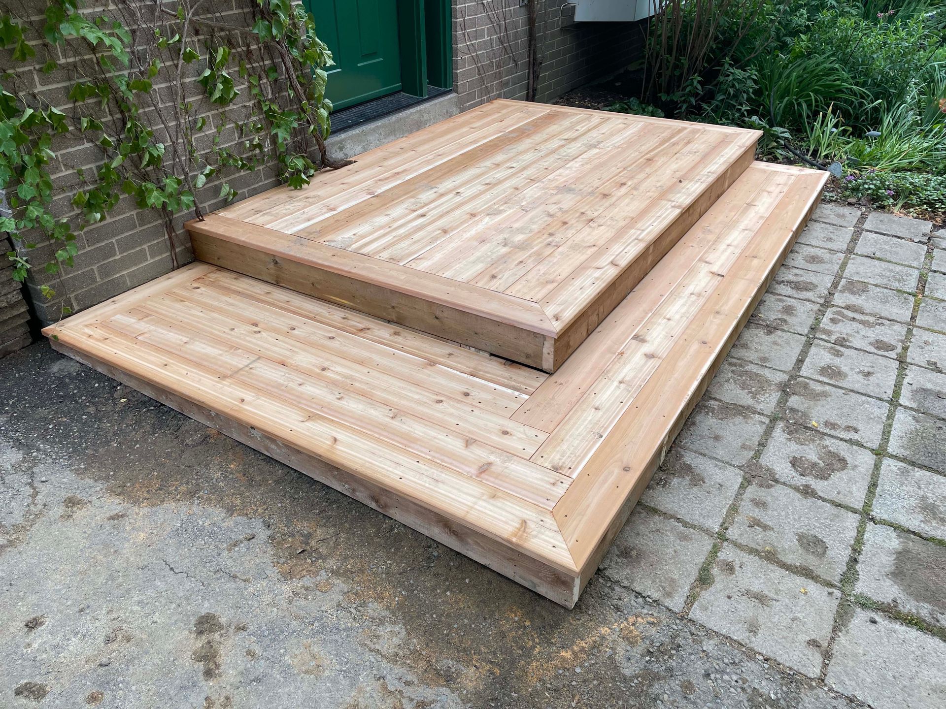 A wooden deck with stairs is sitting on a brick sidewalk in front of a brick building.