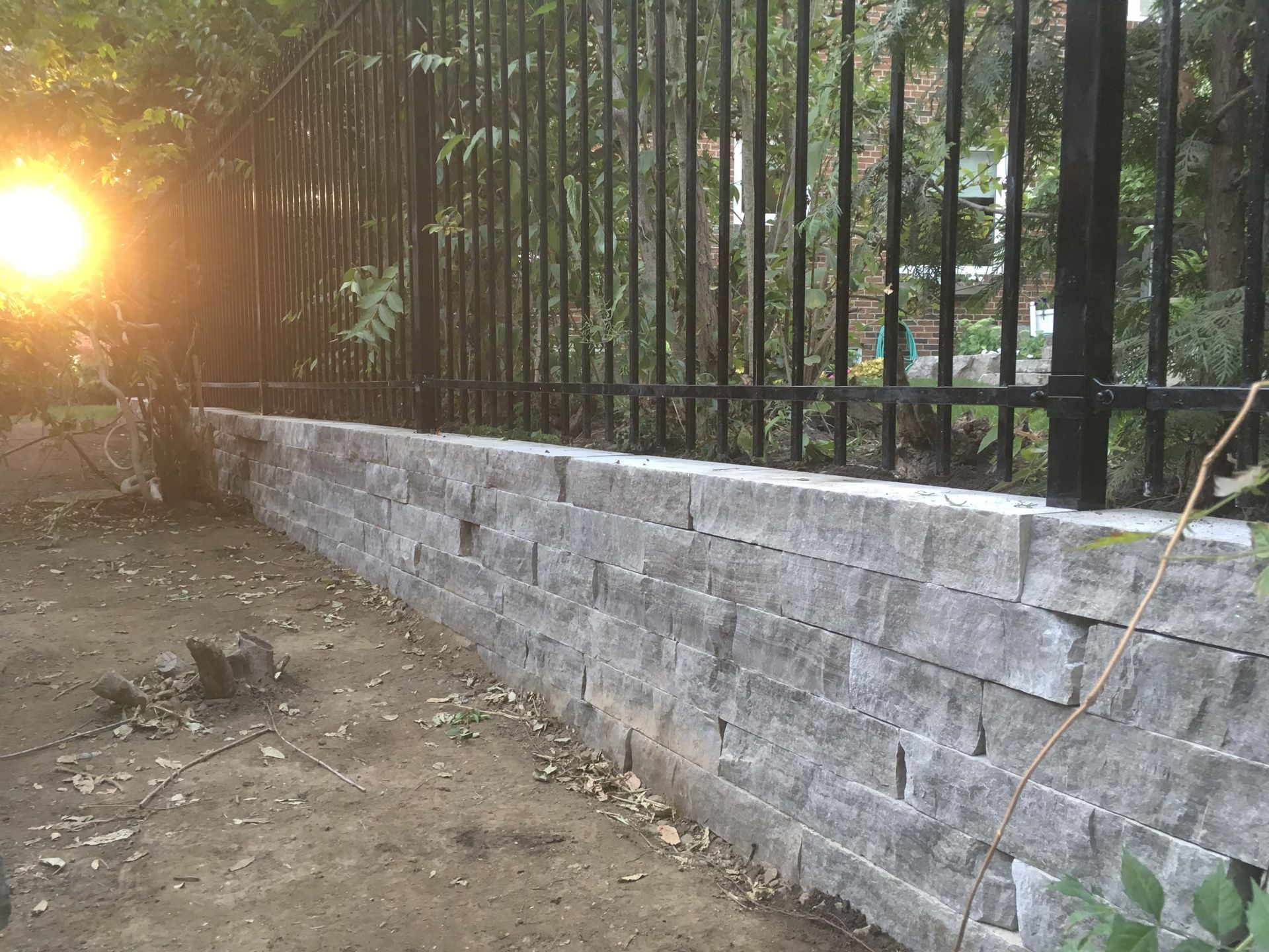 A stone wall with a metal fence behind it.