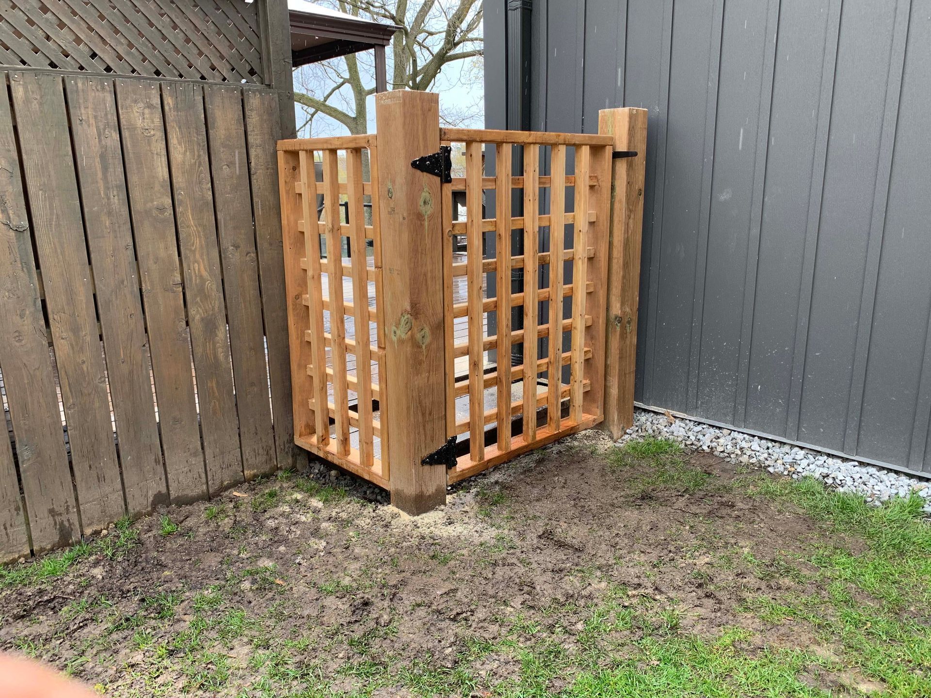 A wooden gate is sitting in the grass next to a wooden fence.