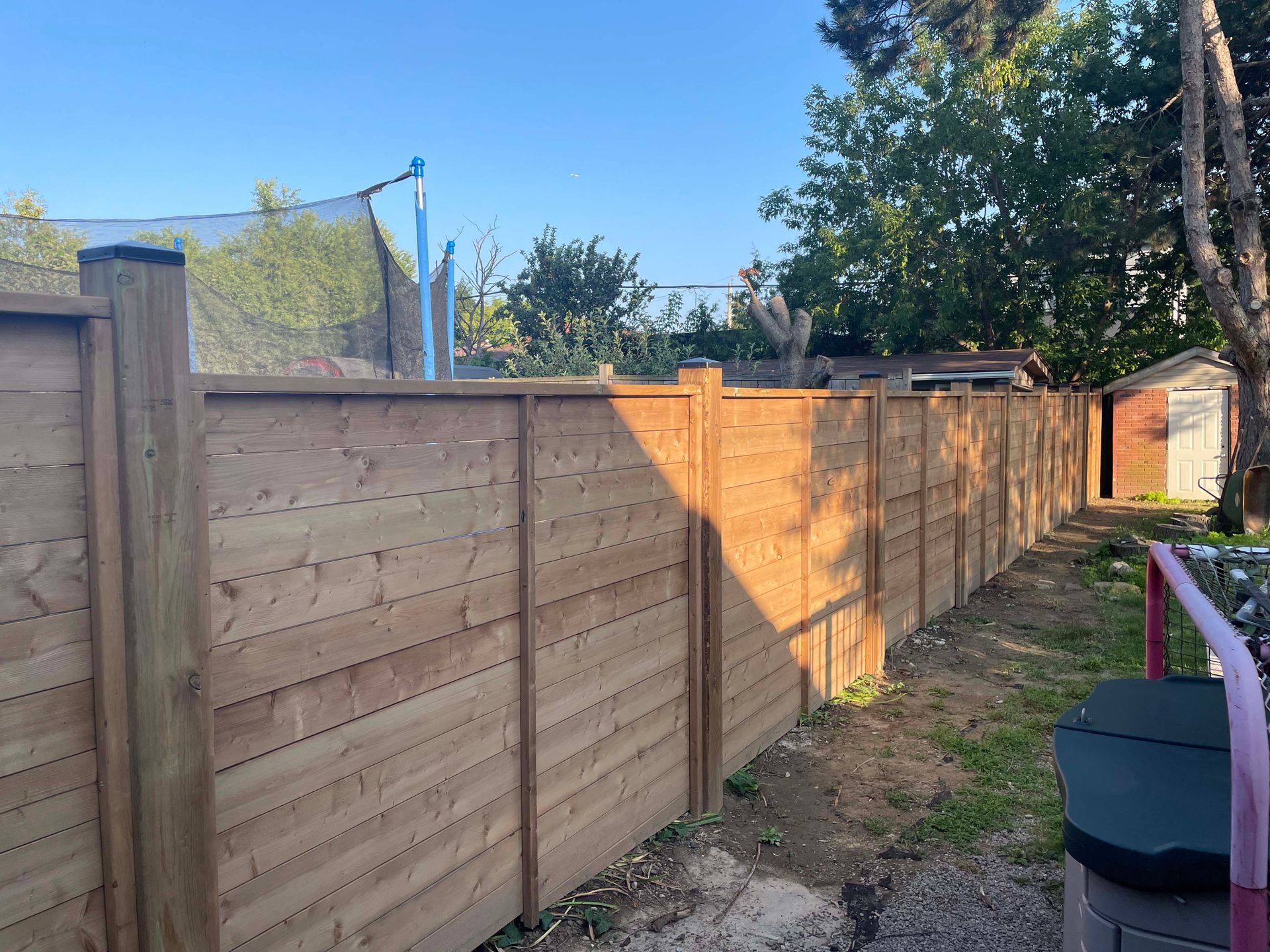 A wooden fence in a backyard with a trampoline in the background.