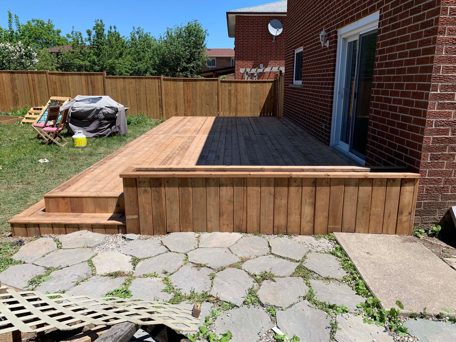 A wooden deck is in the backyard of a brick house.