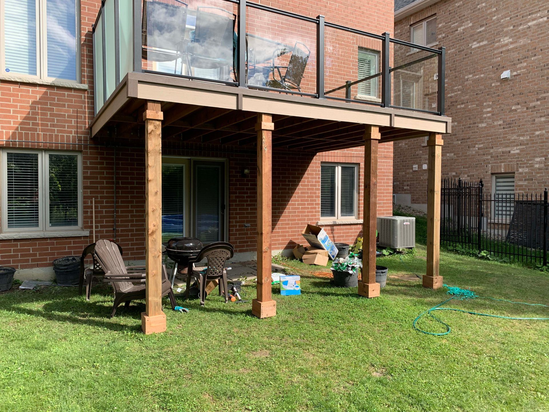 There is a deck with a glass railing in the backyard of a house.