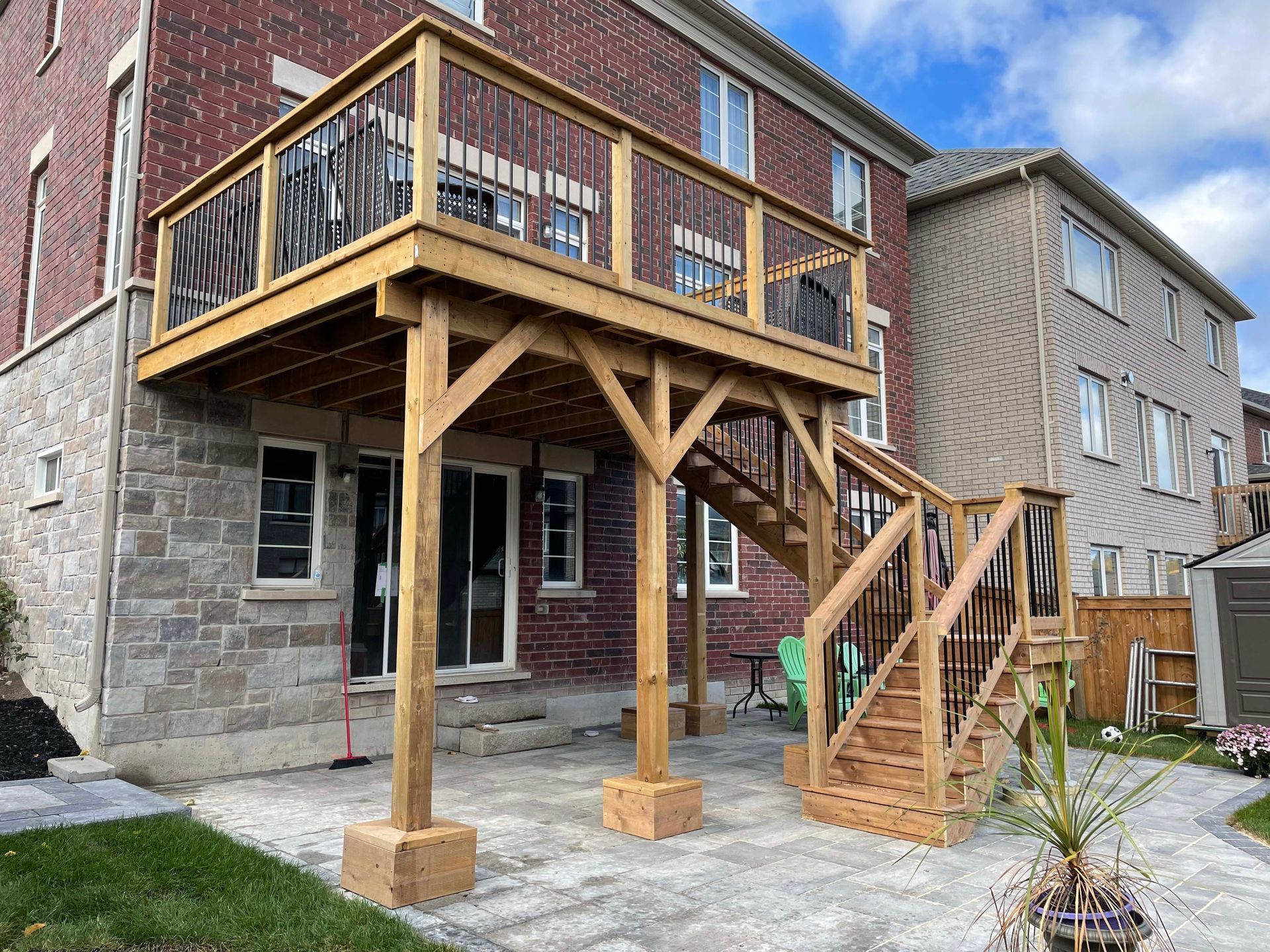 A wooden deck with stairs leading up to it is in front of a brick house.