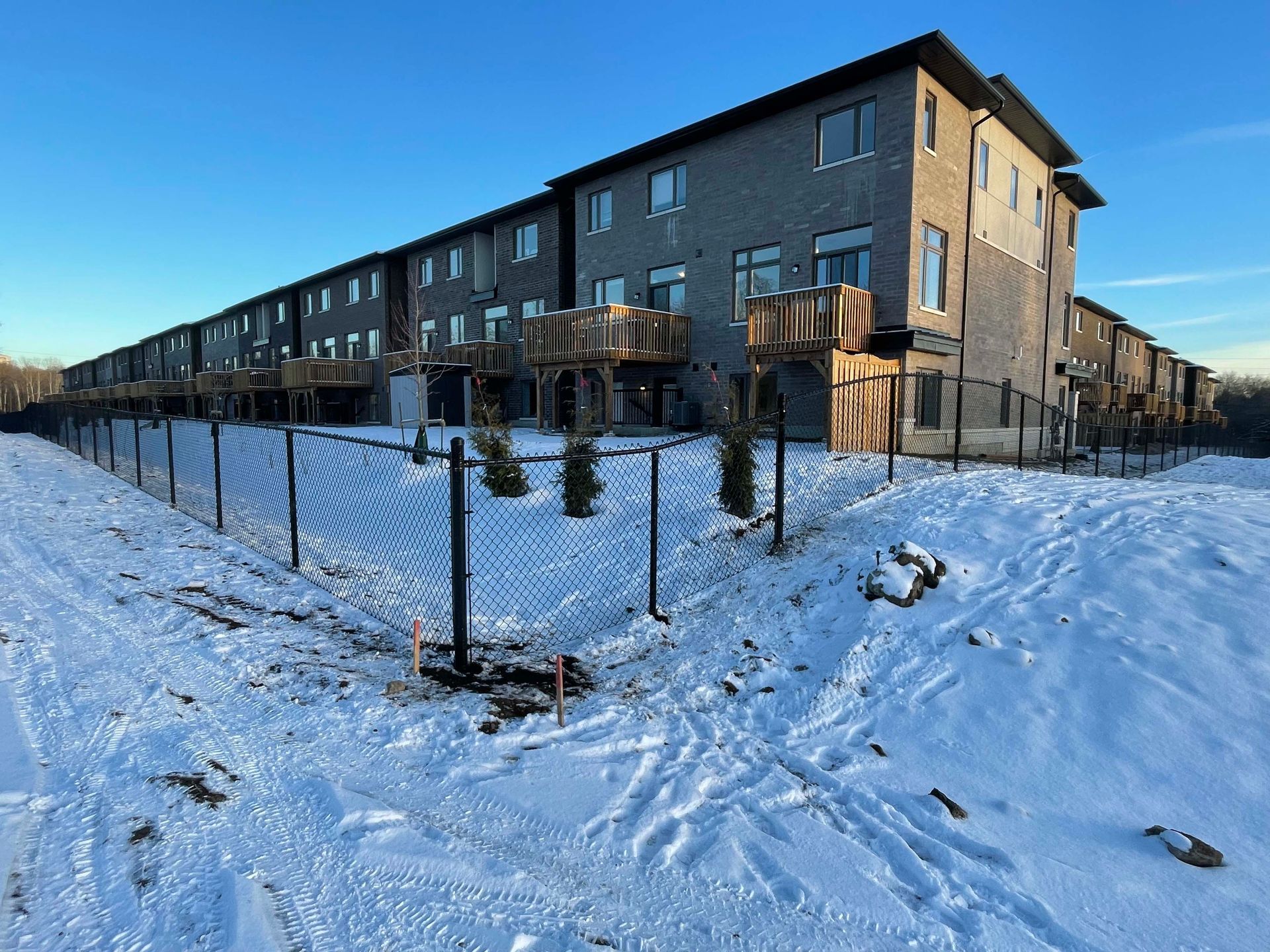 A large apartment building is surrounded by snow and a chain link fence.