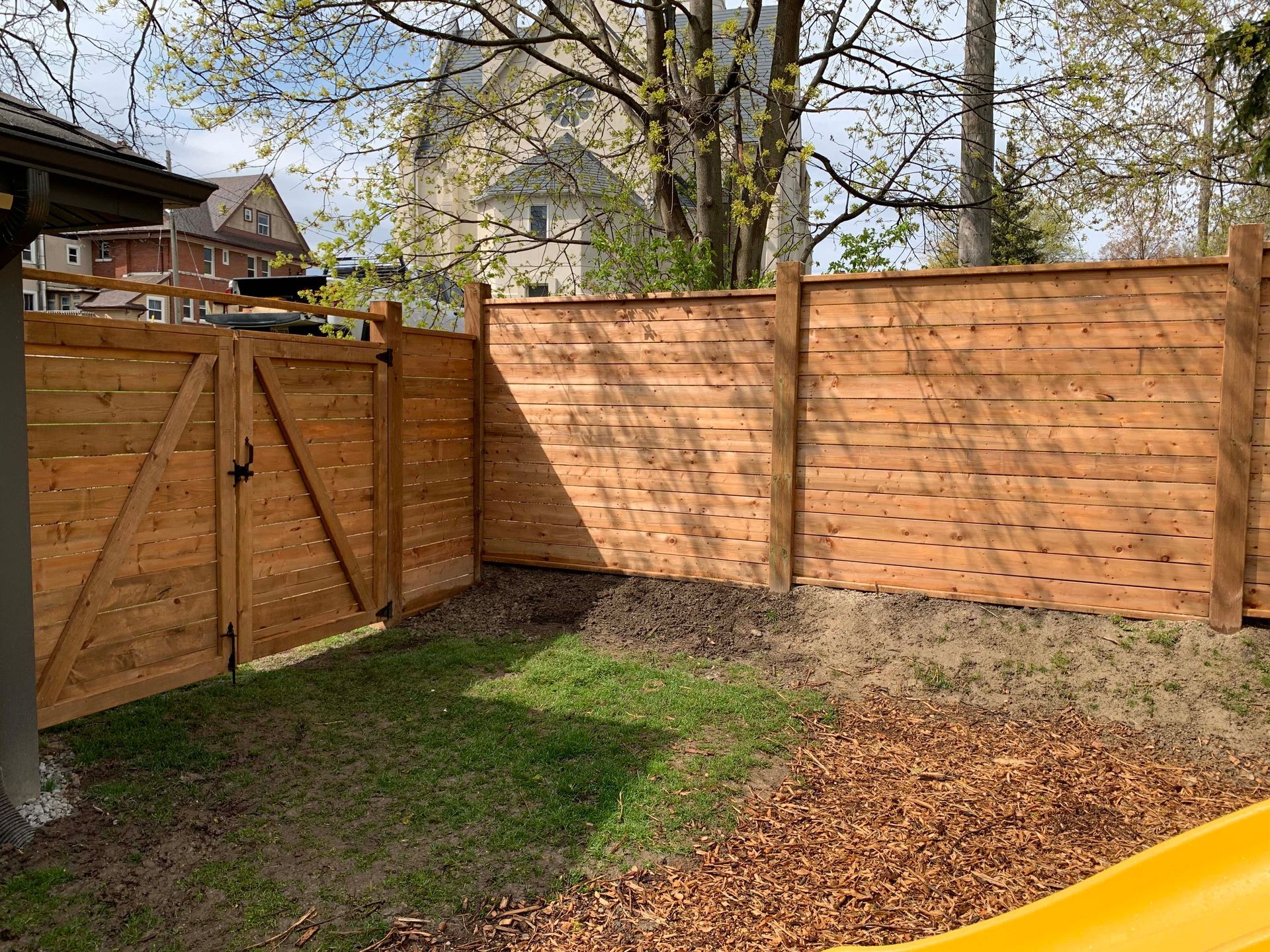 A wooden fence with a gate in a backyard next to a yellow slide.