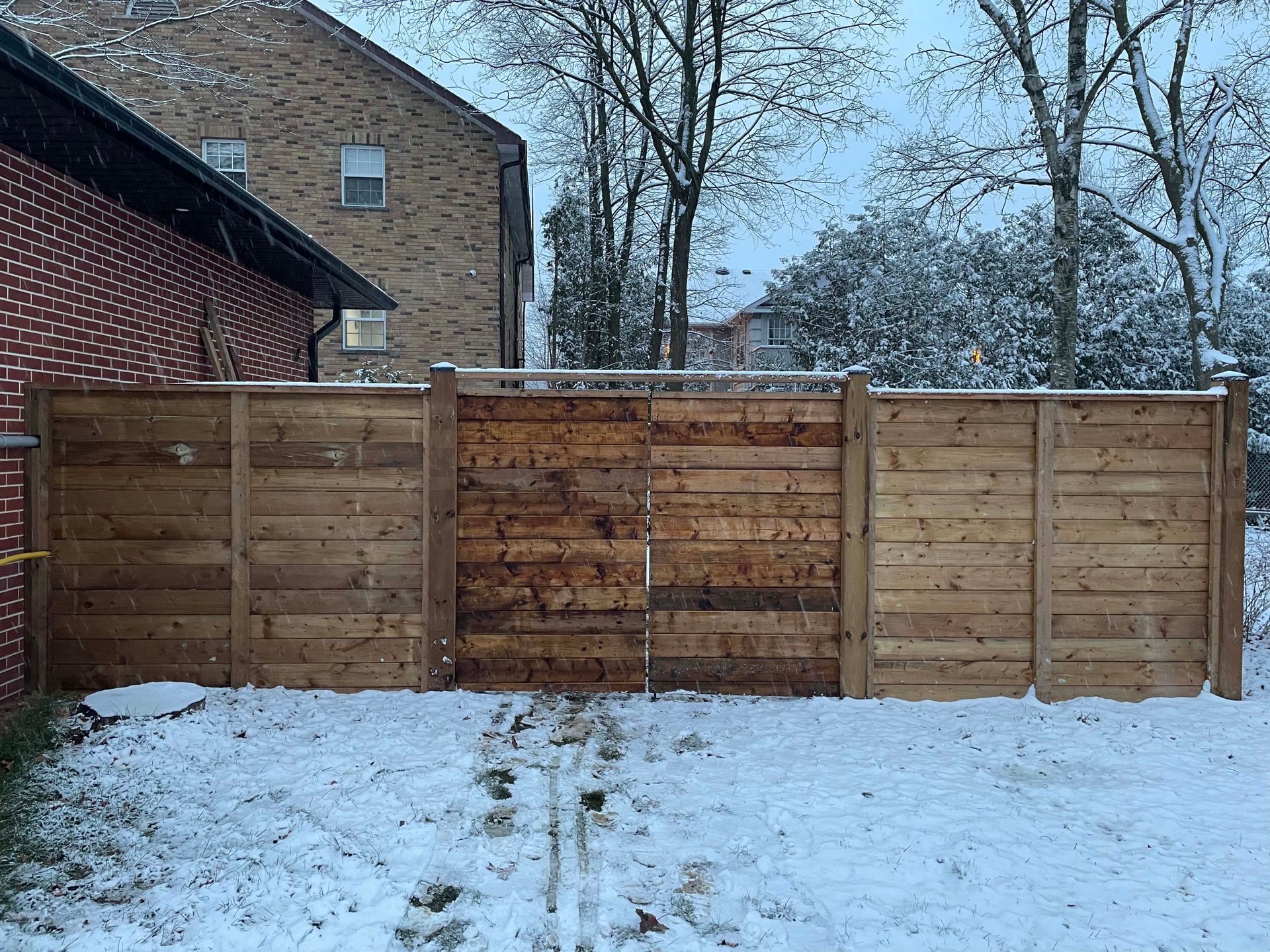 A wooden fence is surrounded by snow in front of a brick building