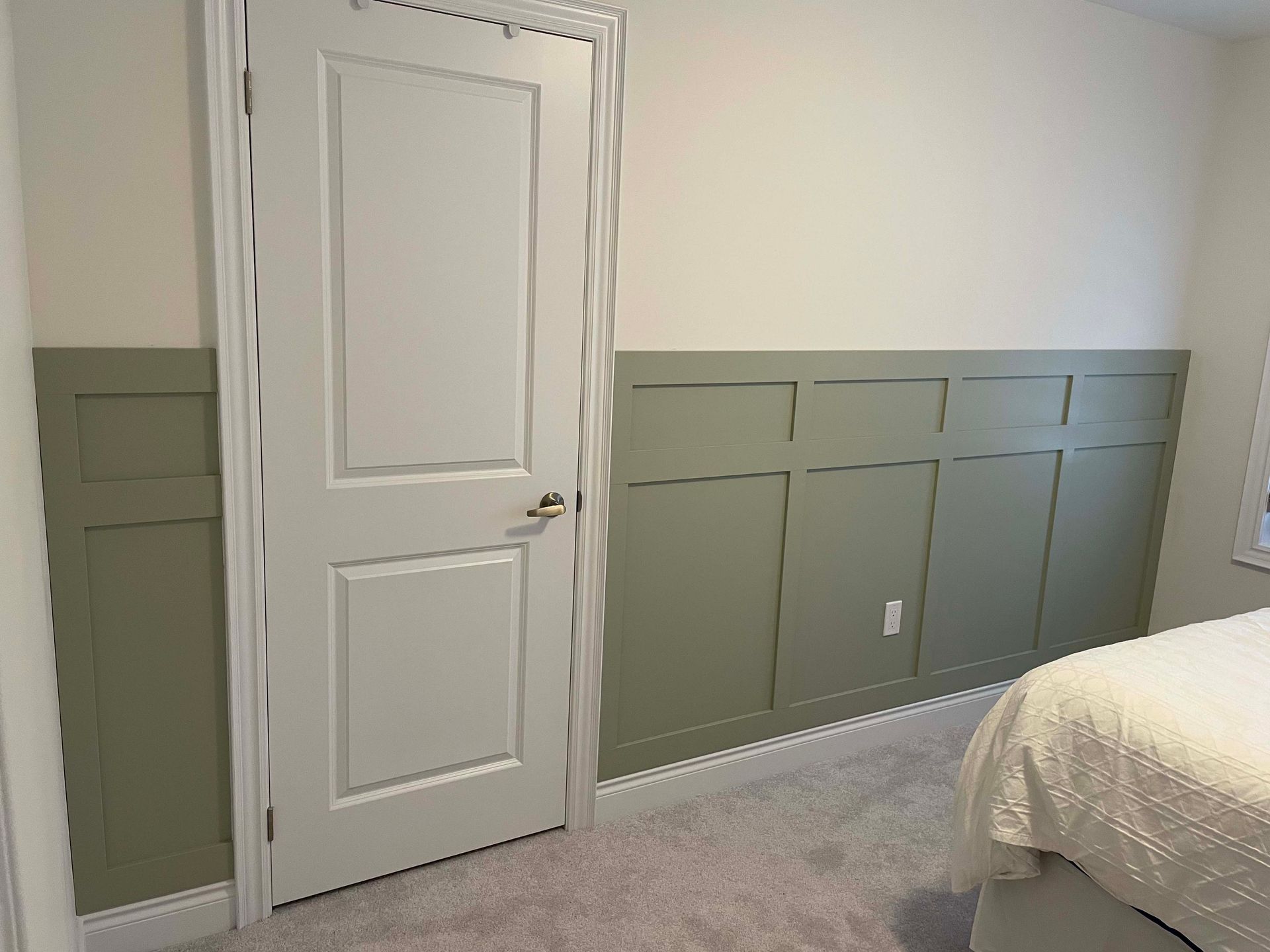 A bedroom with a bed , door , and wall paneling.