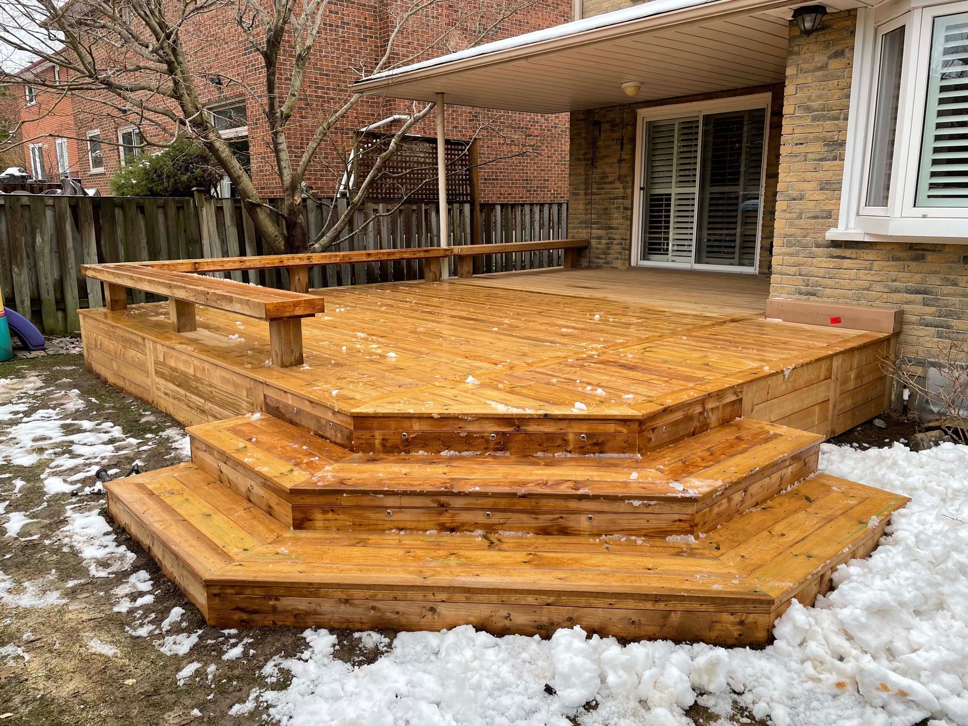 A wooden deck with stairs and benches in the backyard of a house.