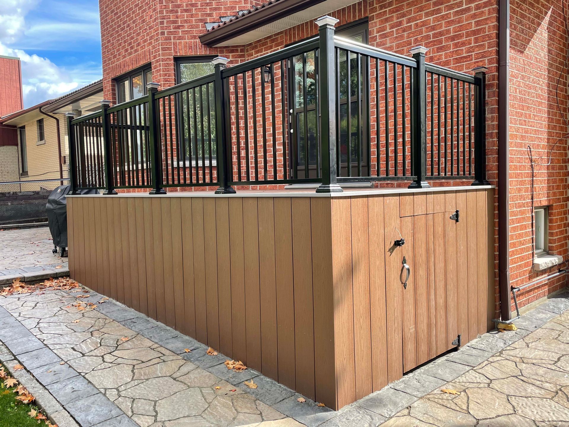 A brick house with a wooden deck and a black railing.