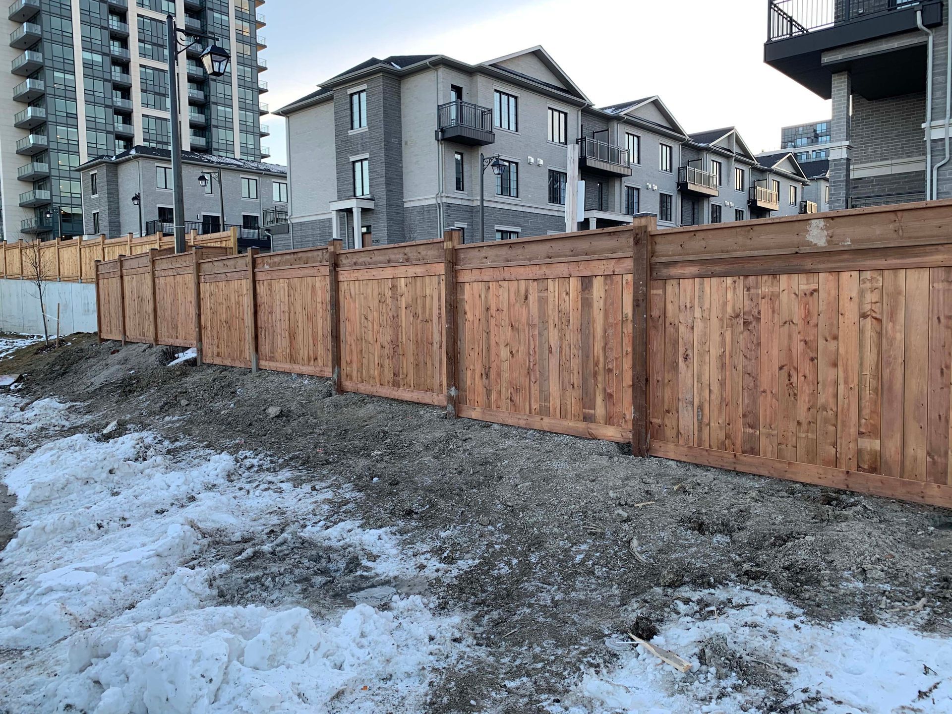 A wooden fence is surrounding a construction site with buildings in the background.