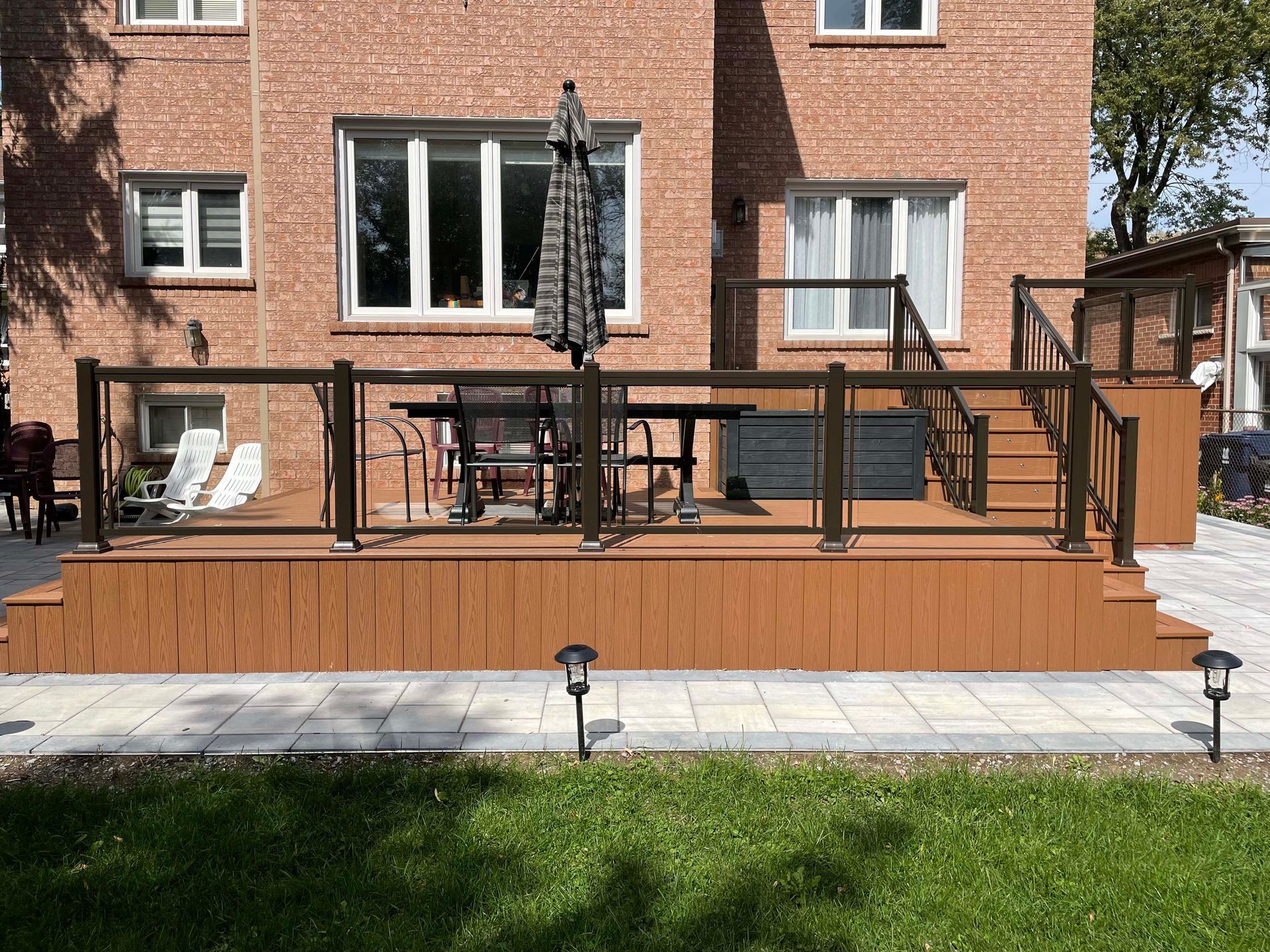 A deck with a table and chairs on it in front of a brick house.