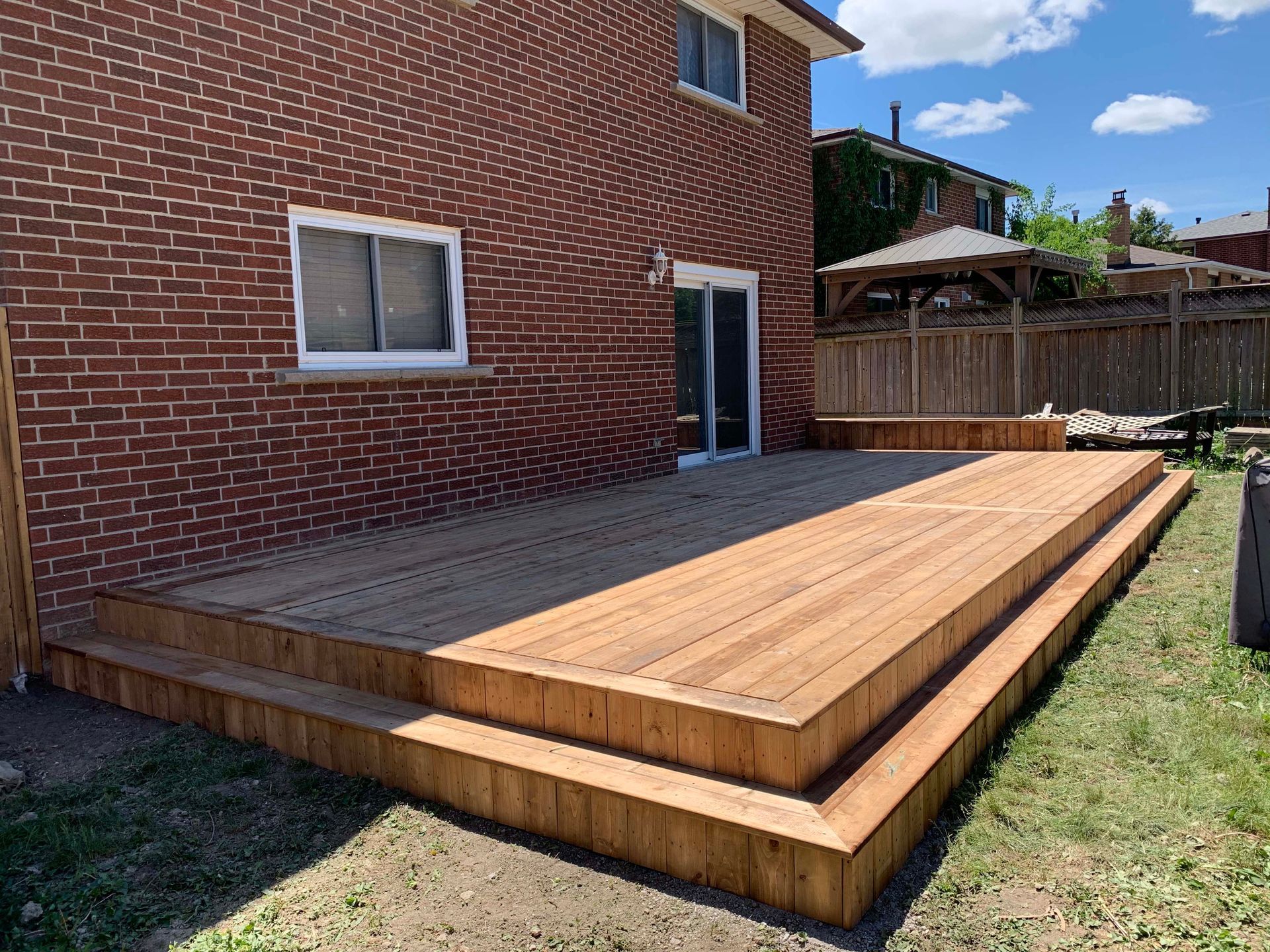 A large wooden deck is in the backyard of a brick house.