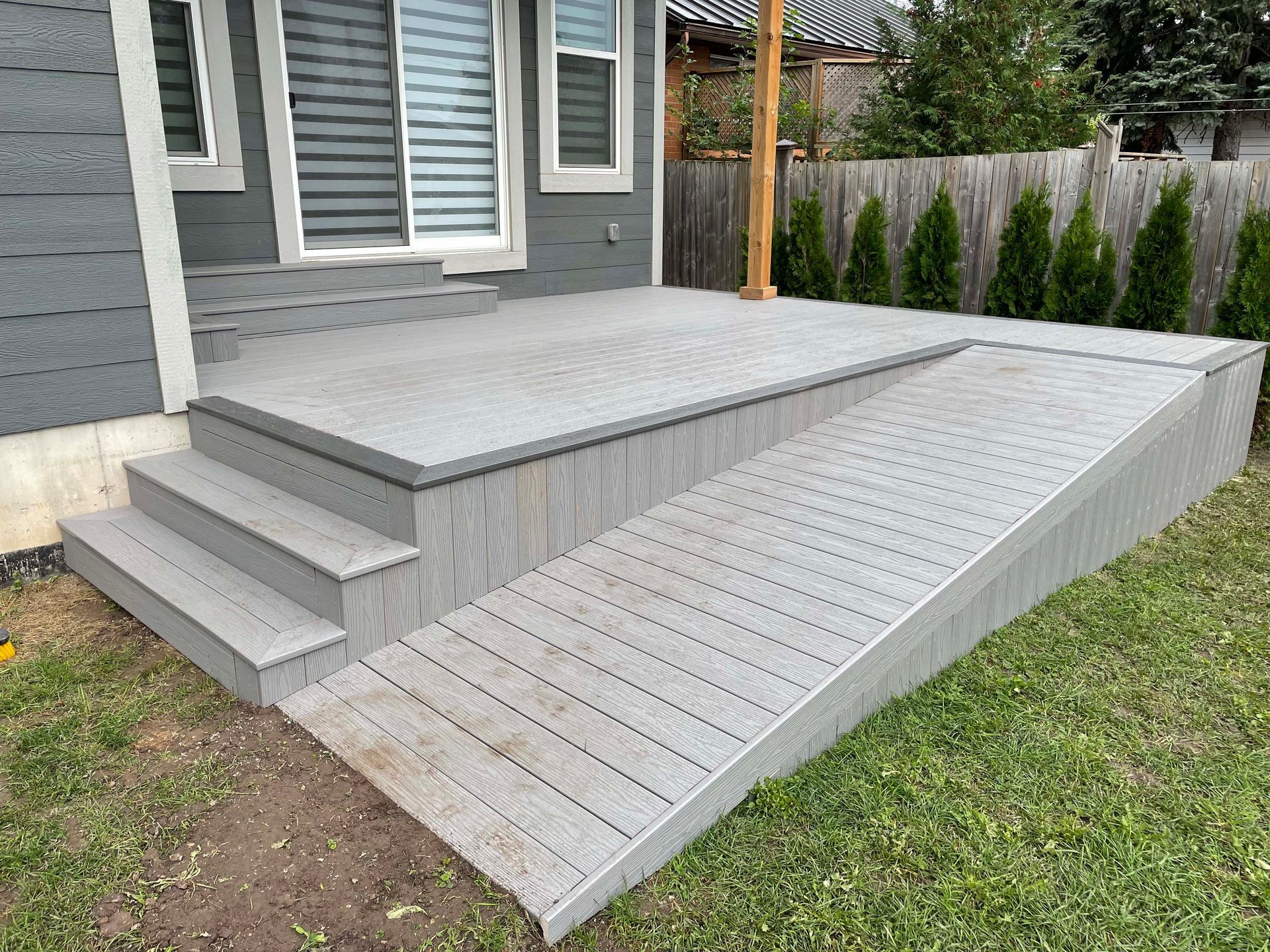 A gray deck with stairs and a ramp in front of a house.