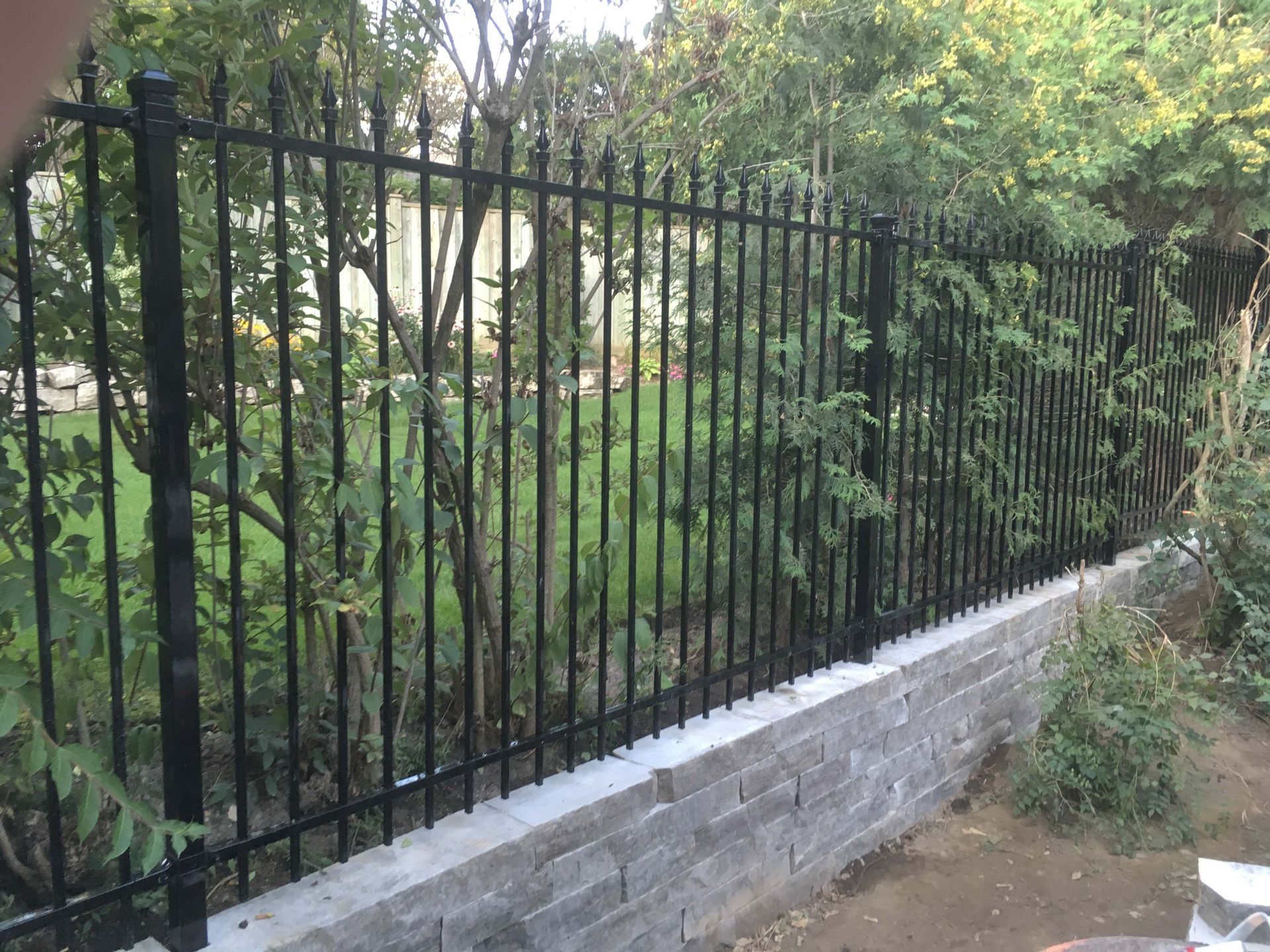 A black wrought iron fence surrounds a stone wall