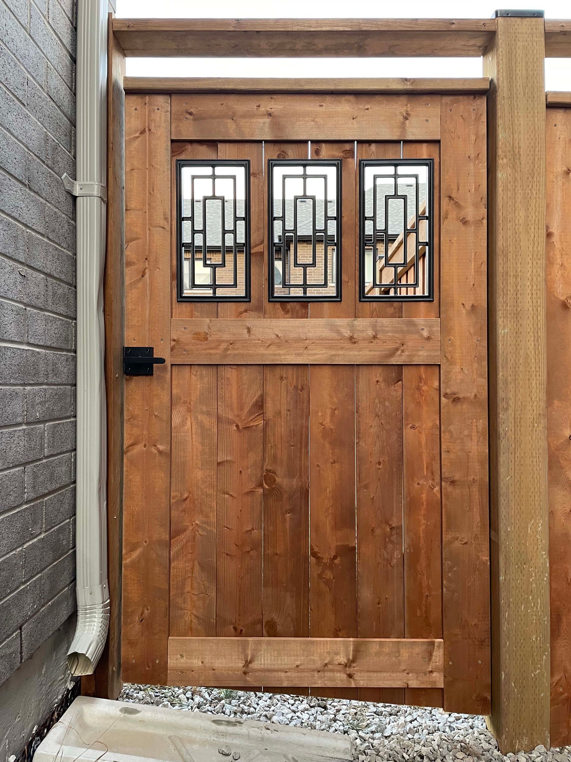 A wooden gate with three windows is next to a brick wall.