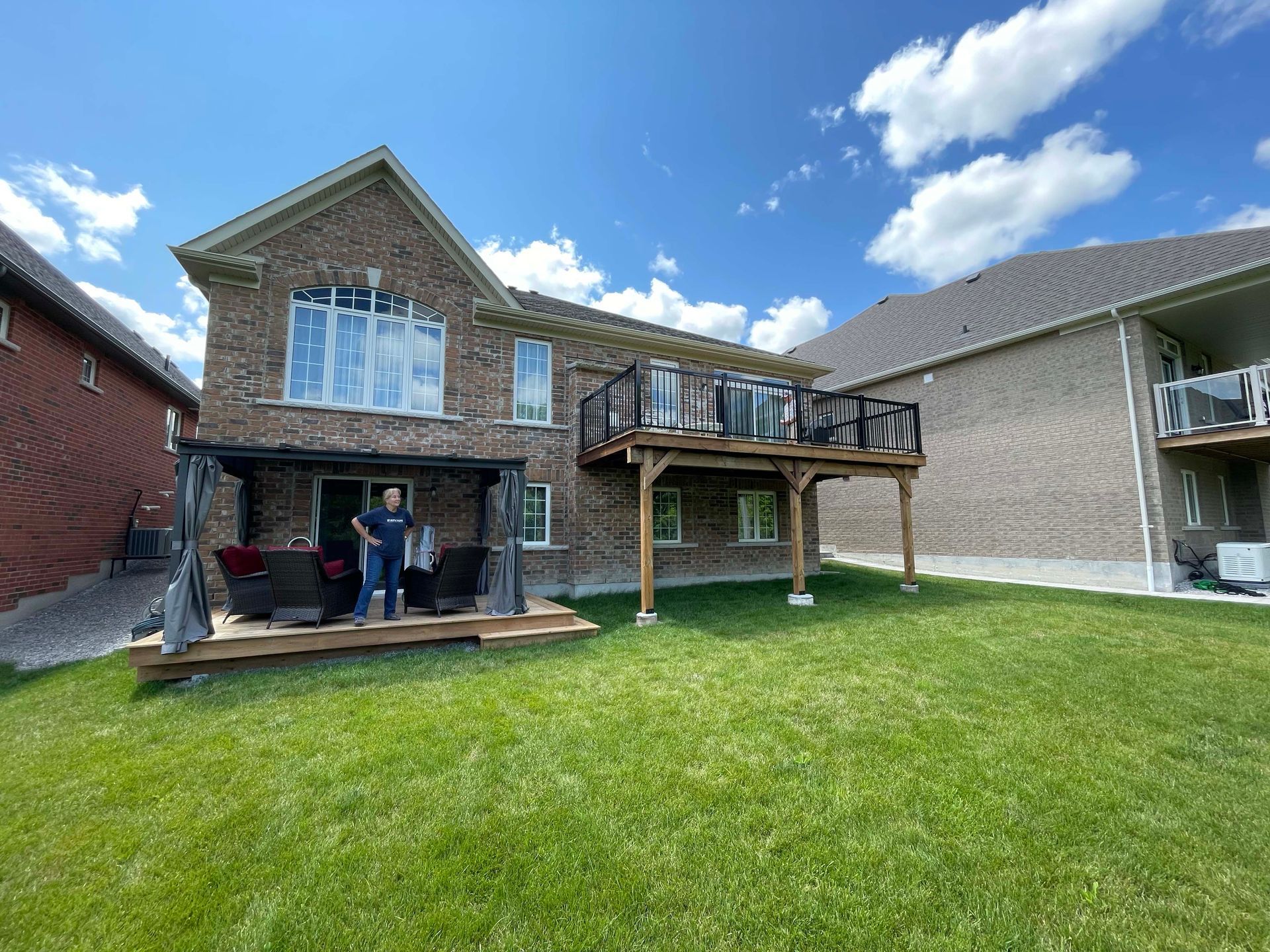 A man is standing on a deck in the backyard of a house.
