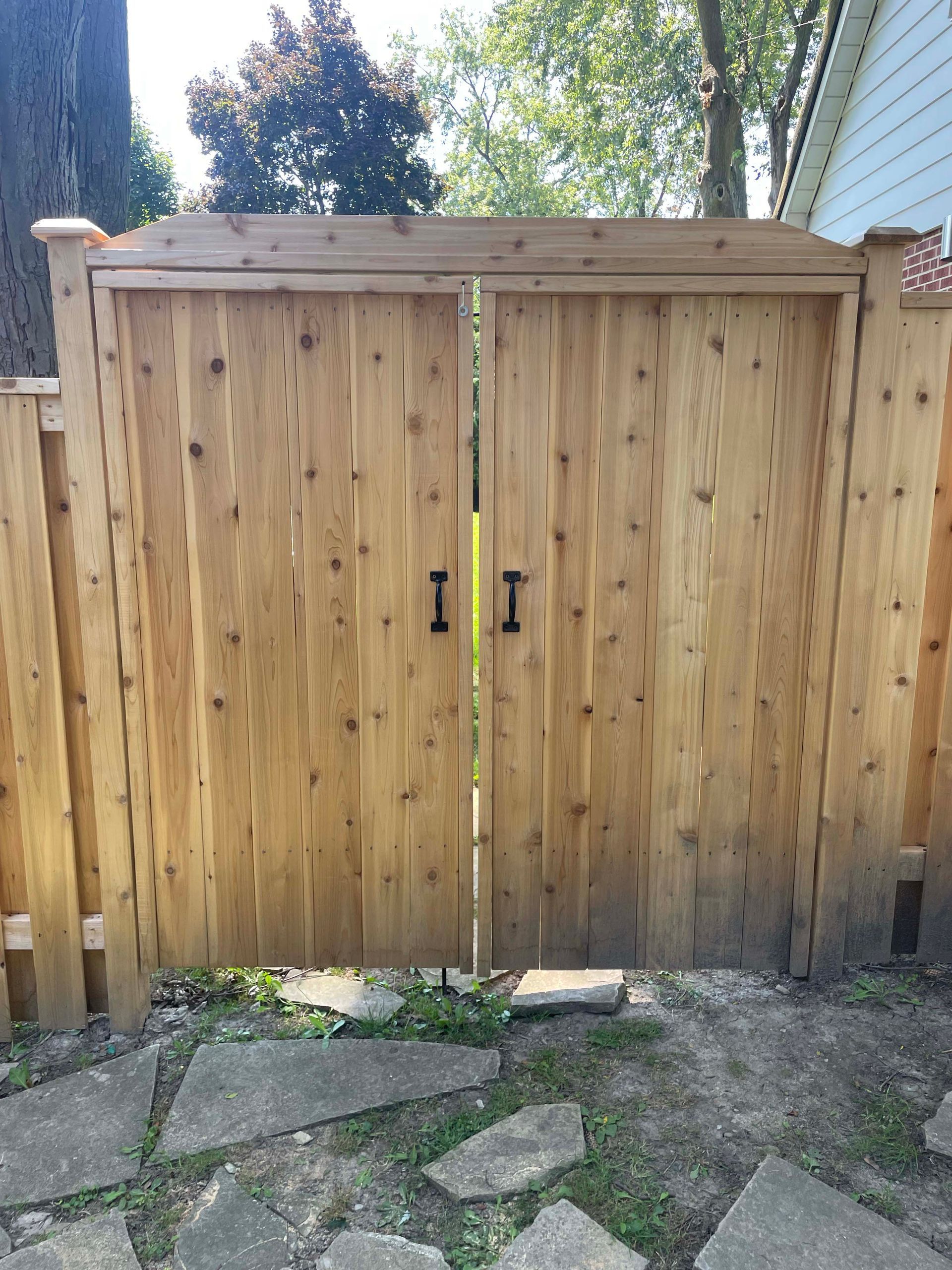 A wooden fence with two doors is surrounded by rocks and grass.