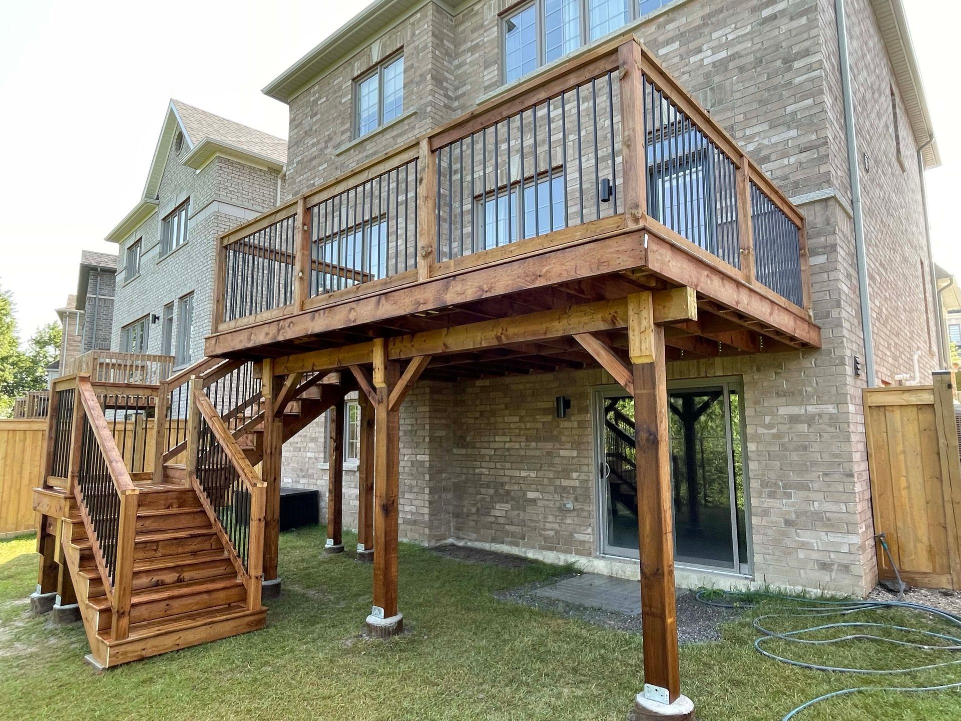 A wooden deck with stairs is in the backyard of a brick house.