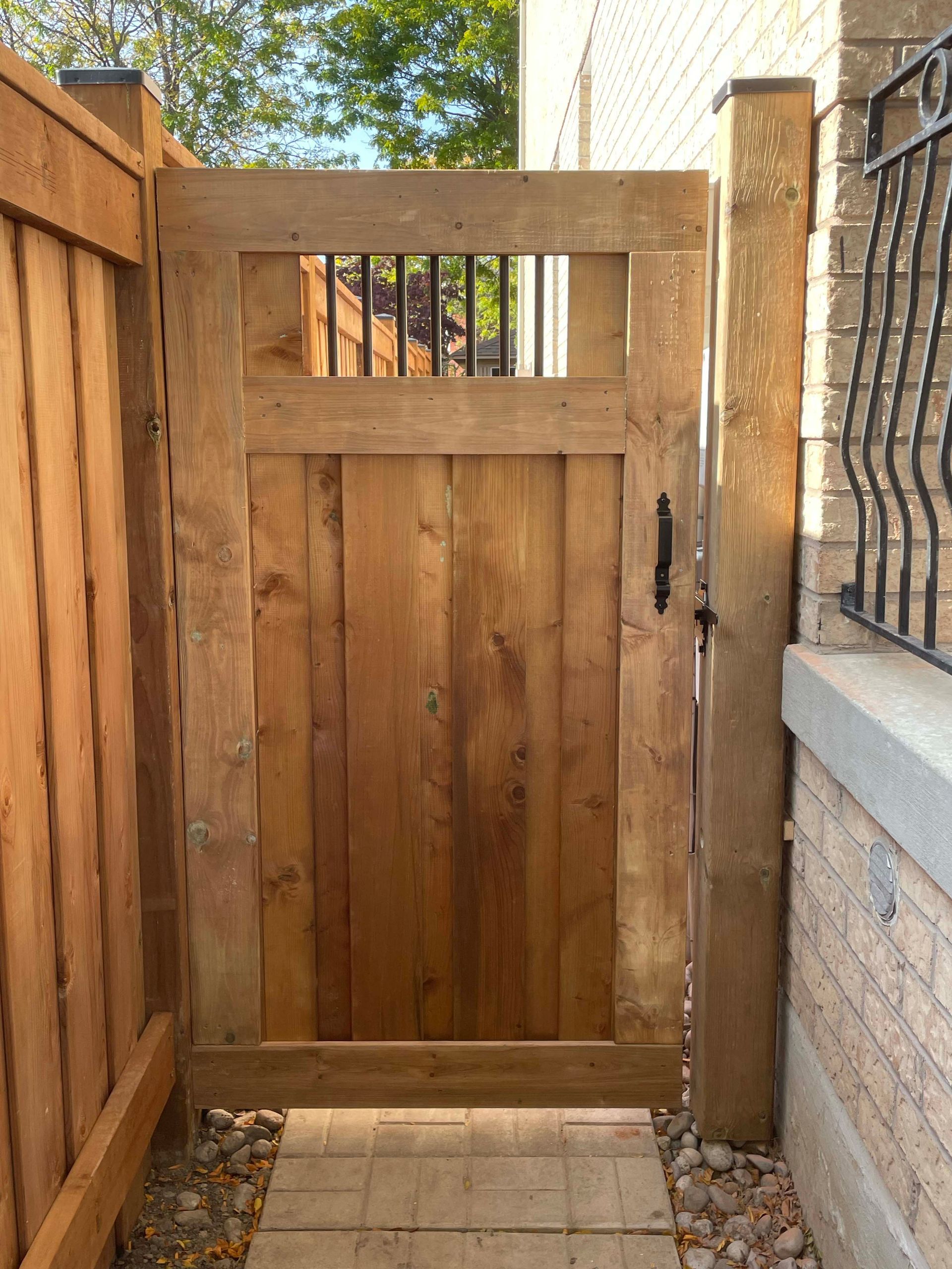 A wooden gate is between a wooden fence and a brick wall.