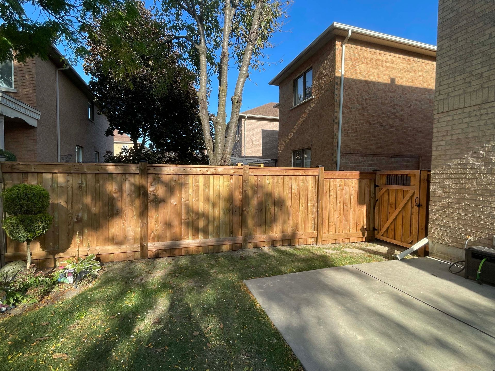 A wooden fence is in the backyard of a brick house.