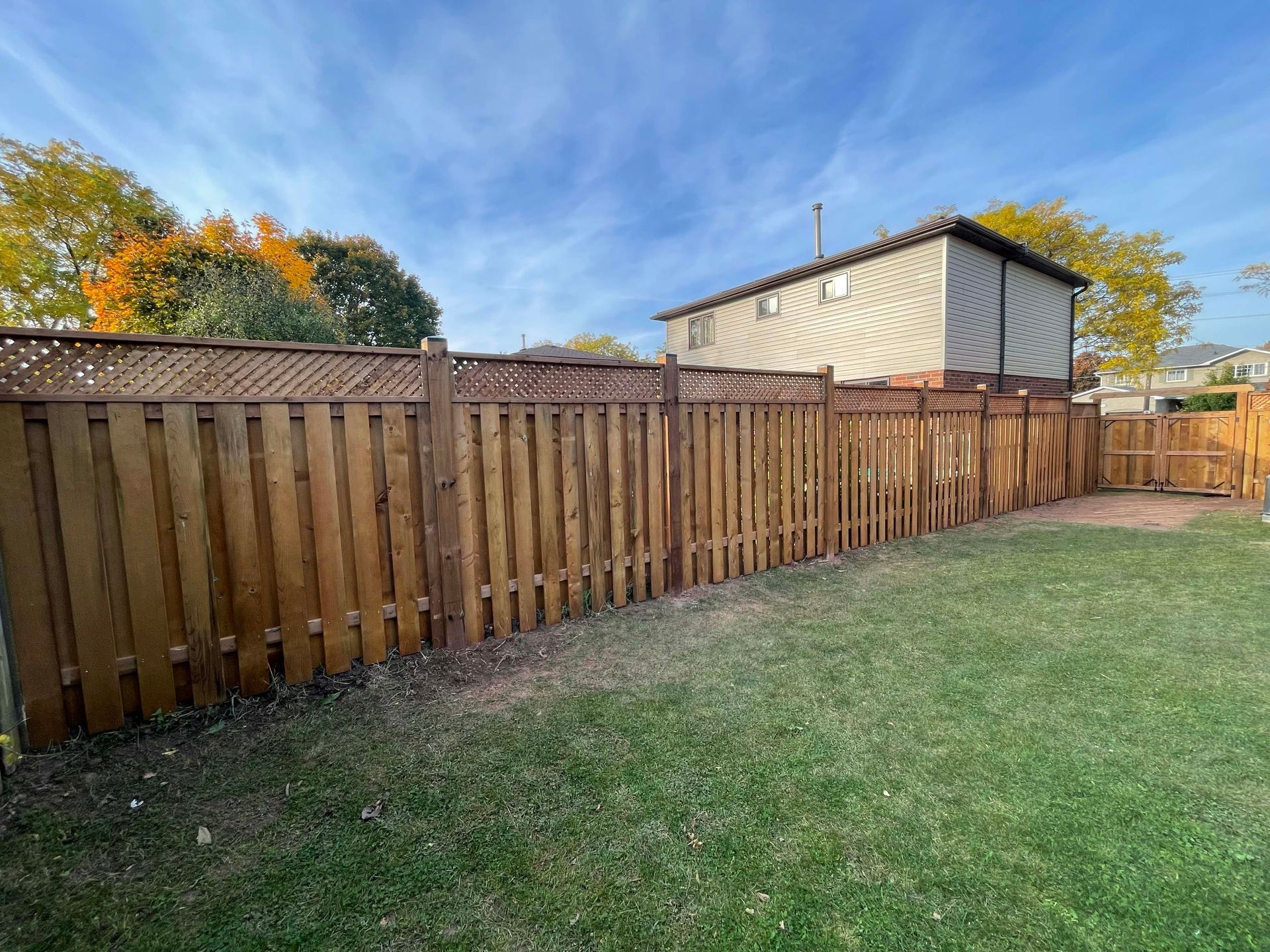 A wooden fence in a backyard with a house in the background.