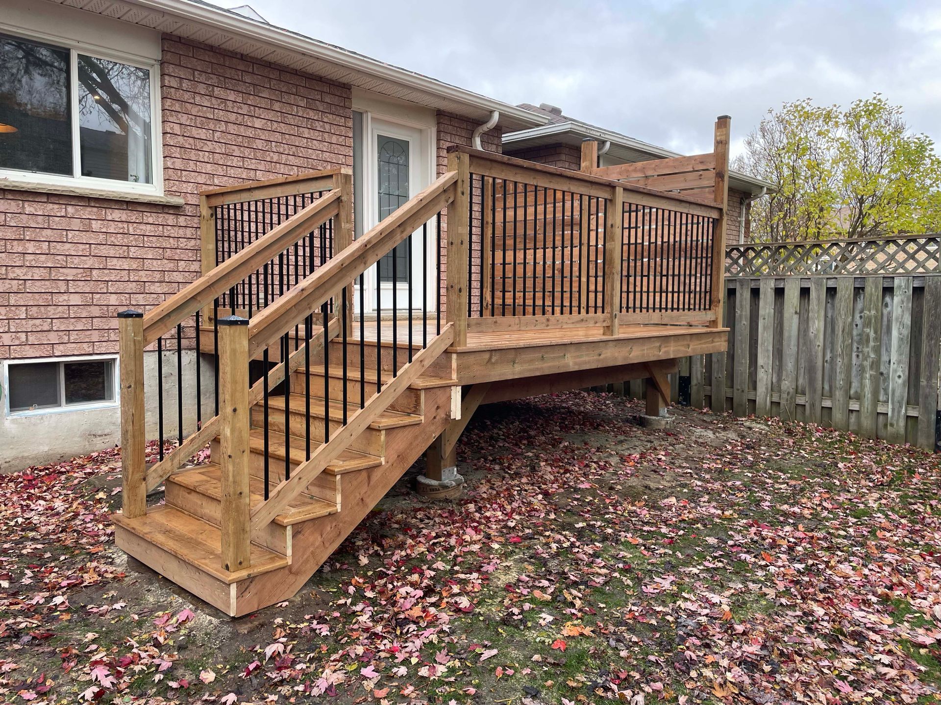 A wooden deck with stairs leading up to it is in the backyard of a house.