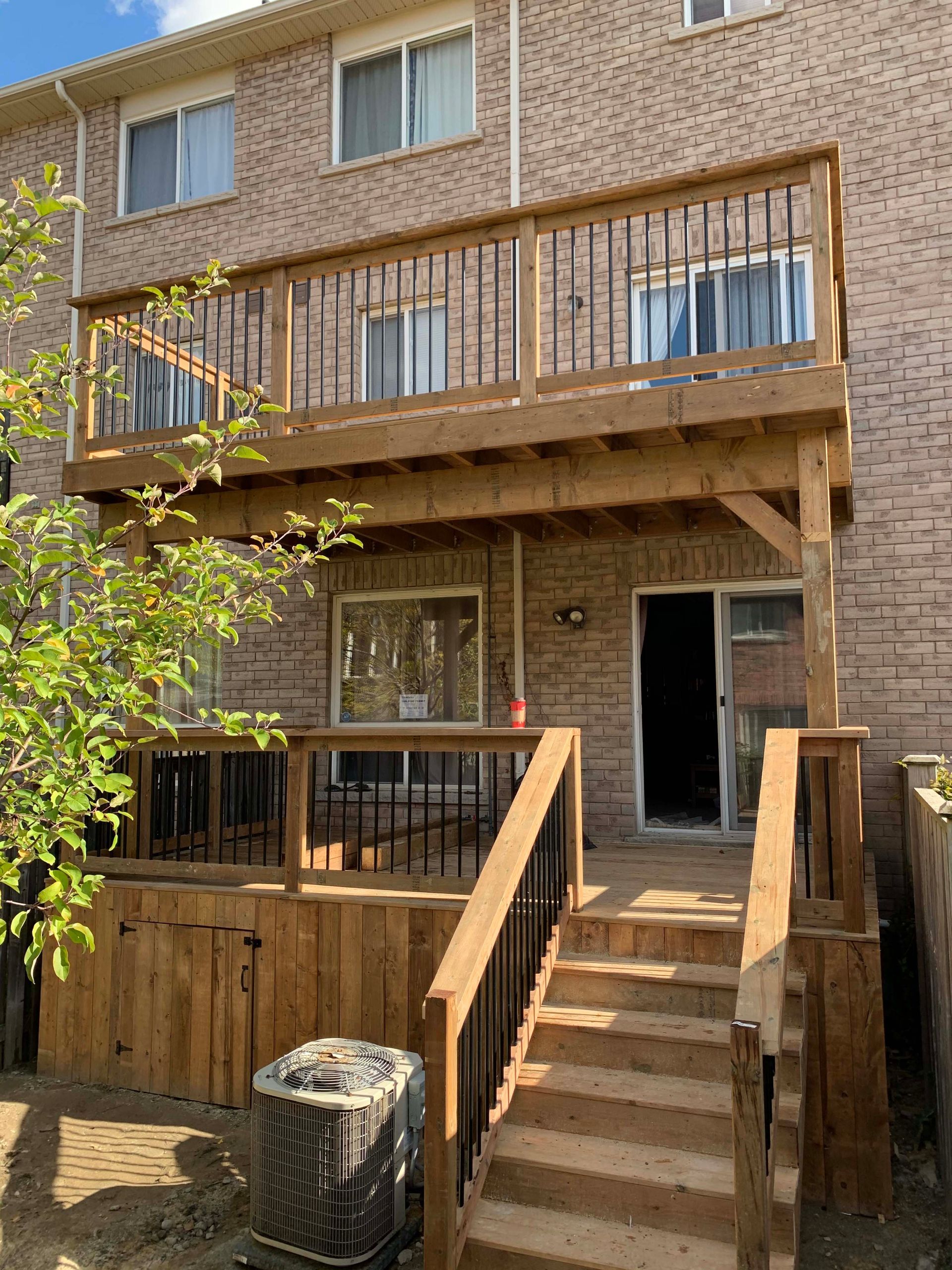 A wooden deck with stairs leading up to it is in front of a brick house.
